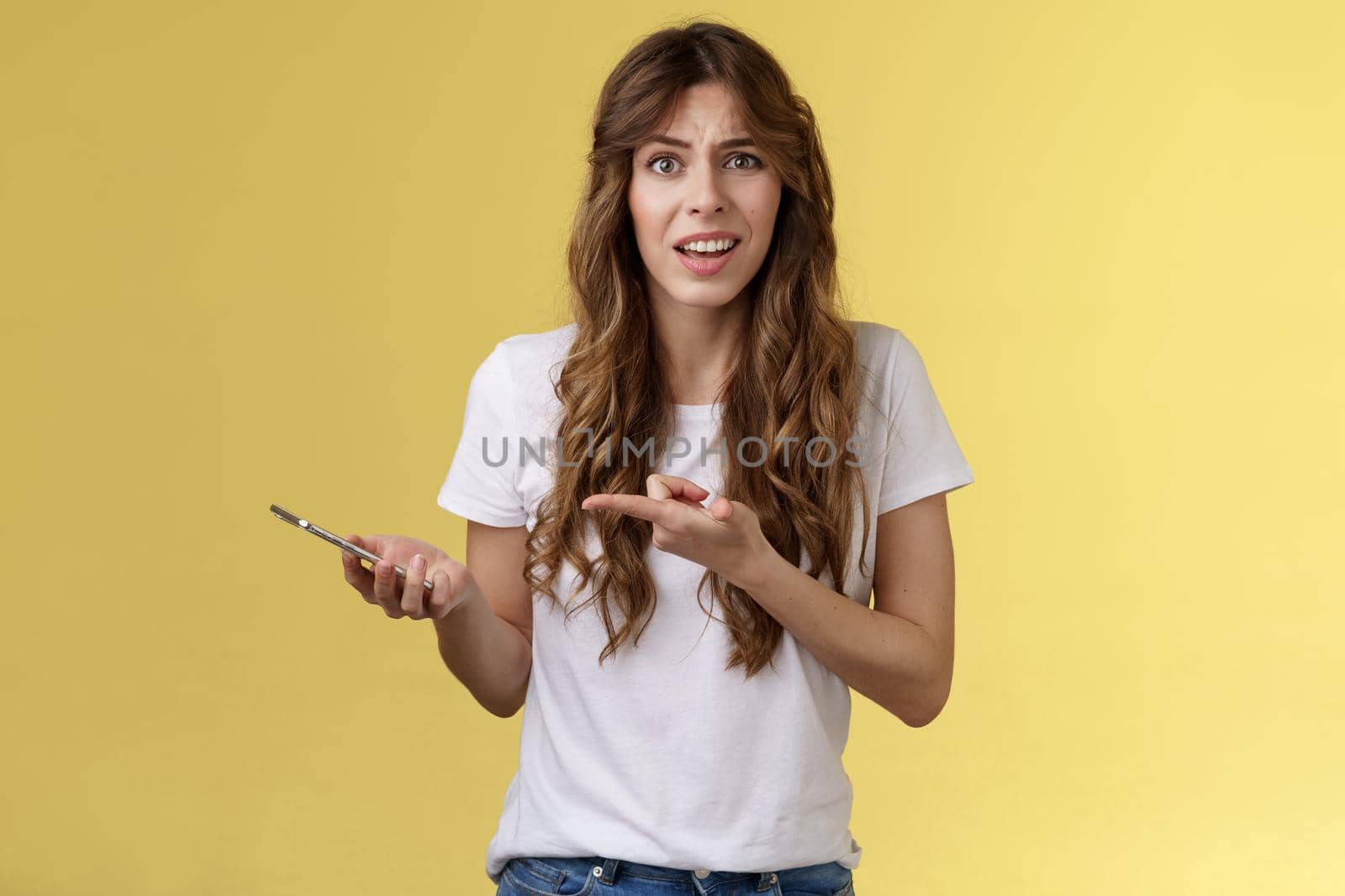 You kidding me. Pissed displeased unsatisfied curly-haired girl frowning grimace bothered look camera complaining bad service finish intense disappointing phone call hold smartphone pointing mobile.