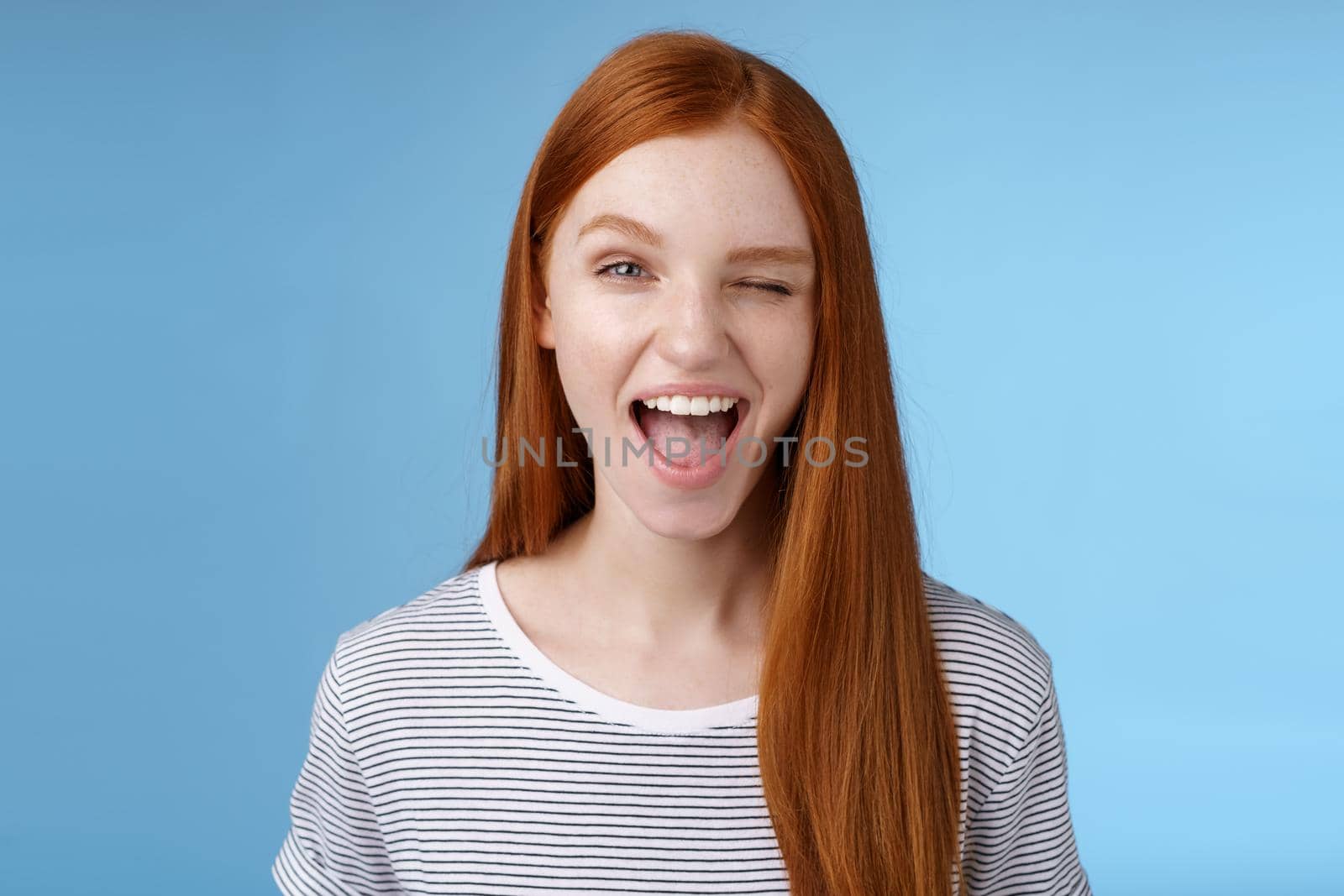 Cheeky good-looking flirty young gorgeous redhead girlfriend winking sassy smiling delighted open mouth hinting have interesting suggestion keep secret standing amused blue background.