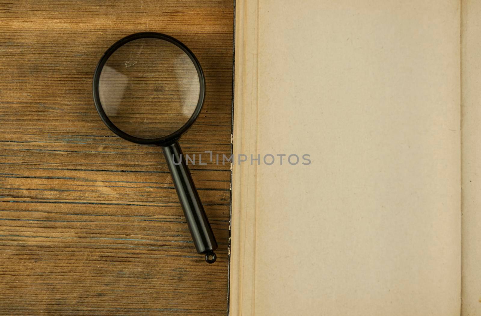 Magnifying lens with open book on wood desk. Start from scratch concept.