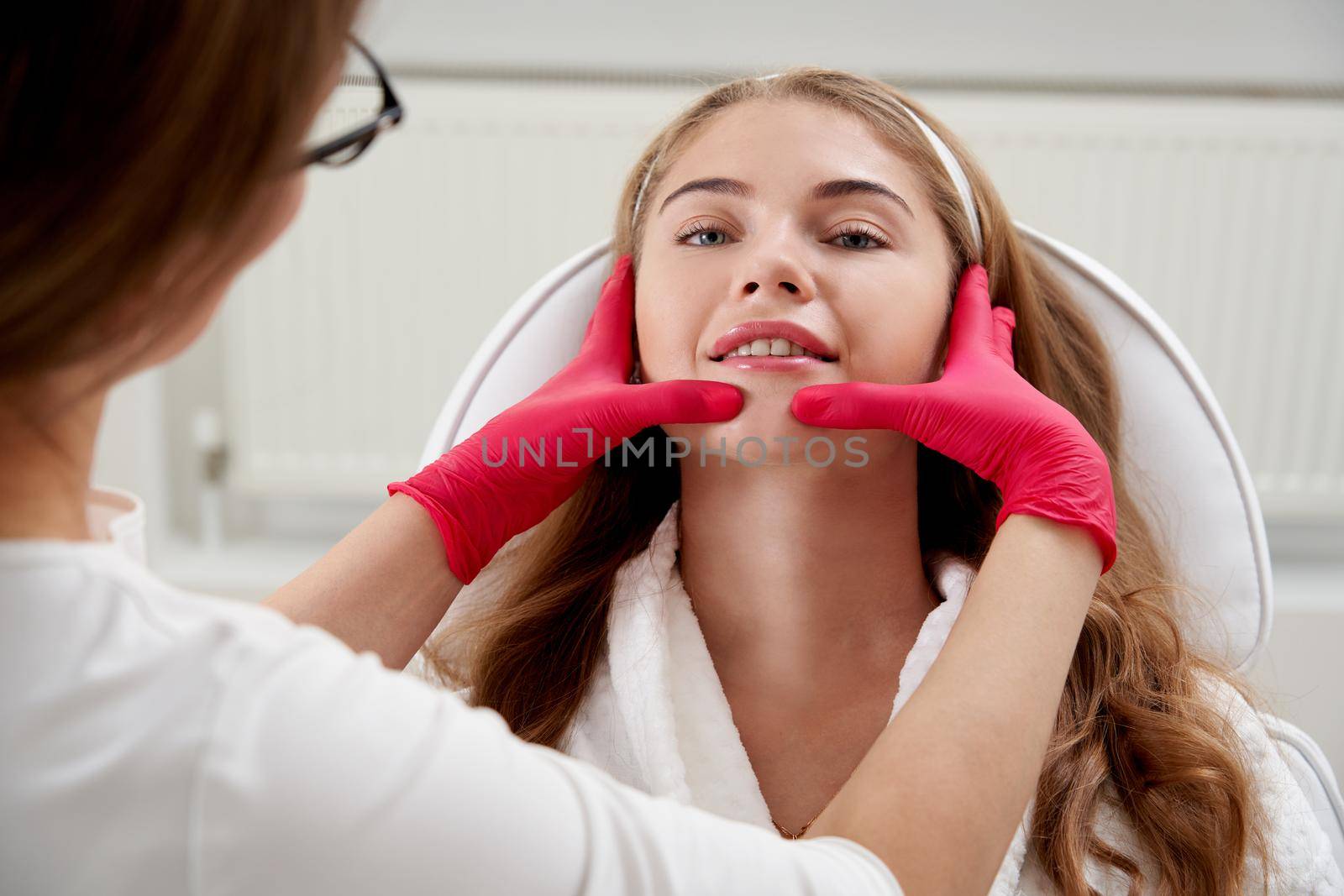 Cosmetologist touching the clients chin in beauty clinic. Beautiful young woman receiving head massage