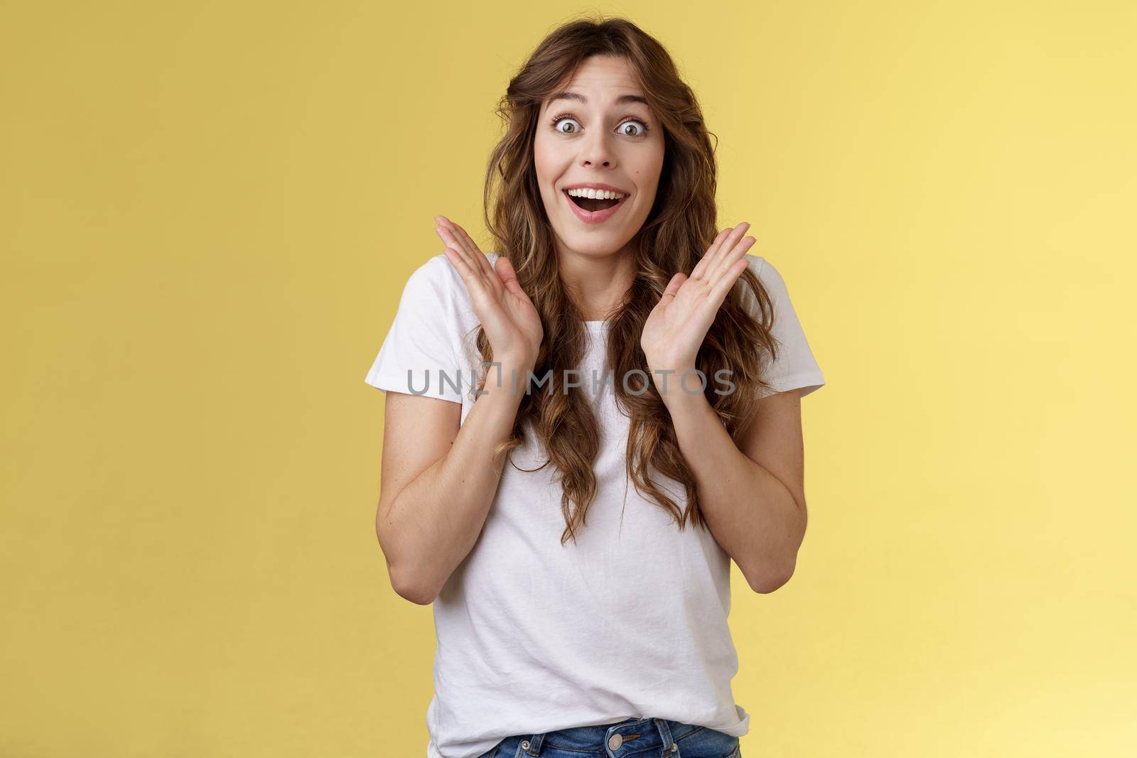Surprised happy pleased impressed curly-haired girl gaze camera admiration satisfaction joy clap hands cheerful smiling broadly look camera fascinated enthusiastic applause yellow background.