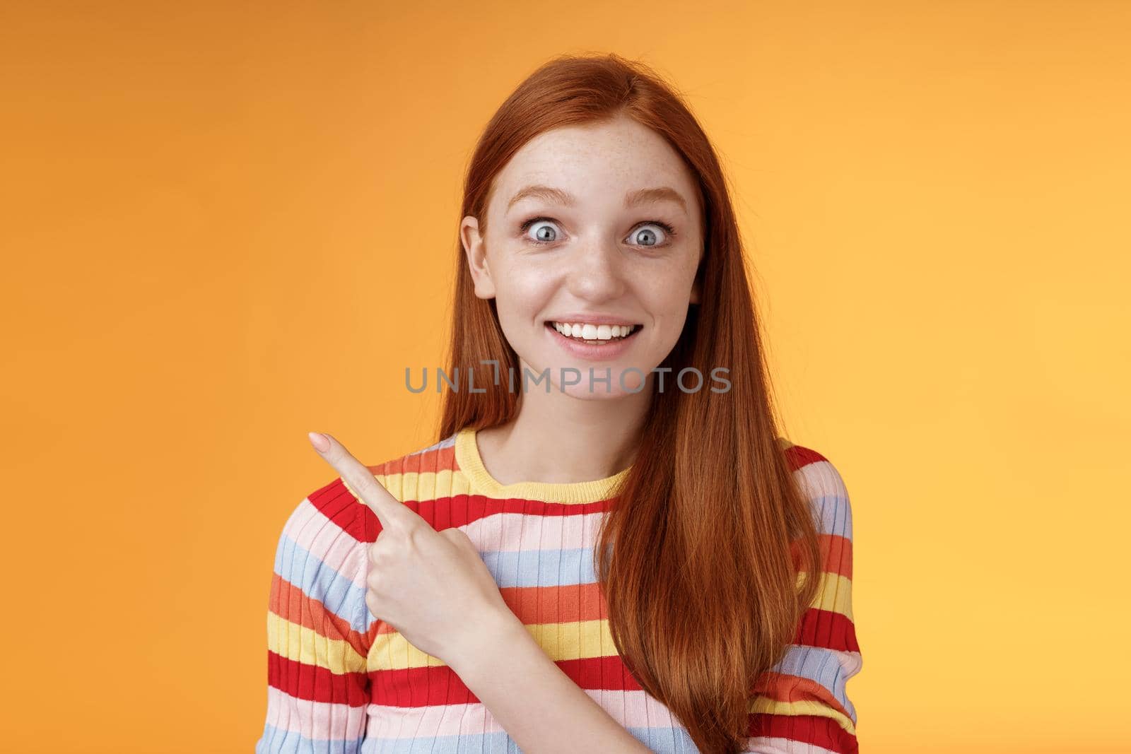 Excited thrilled good-looking young silly redhead girl surprised pop eyes camera gasping impressed pointing upper left corner see super star grinning excitement delight, orange background by Benzoix