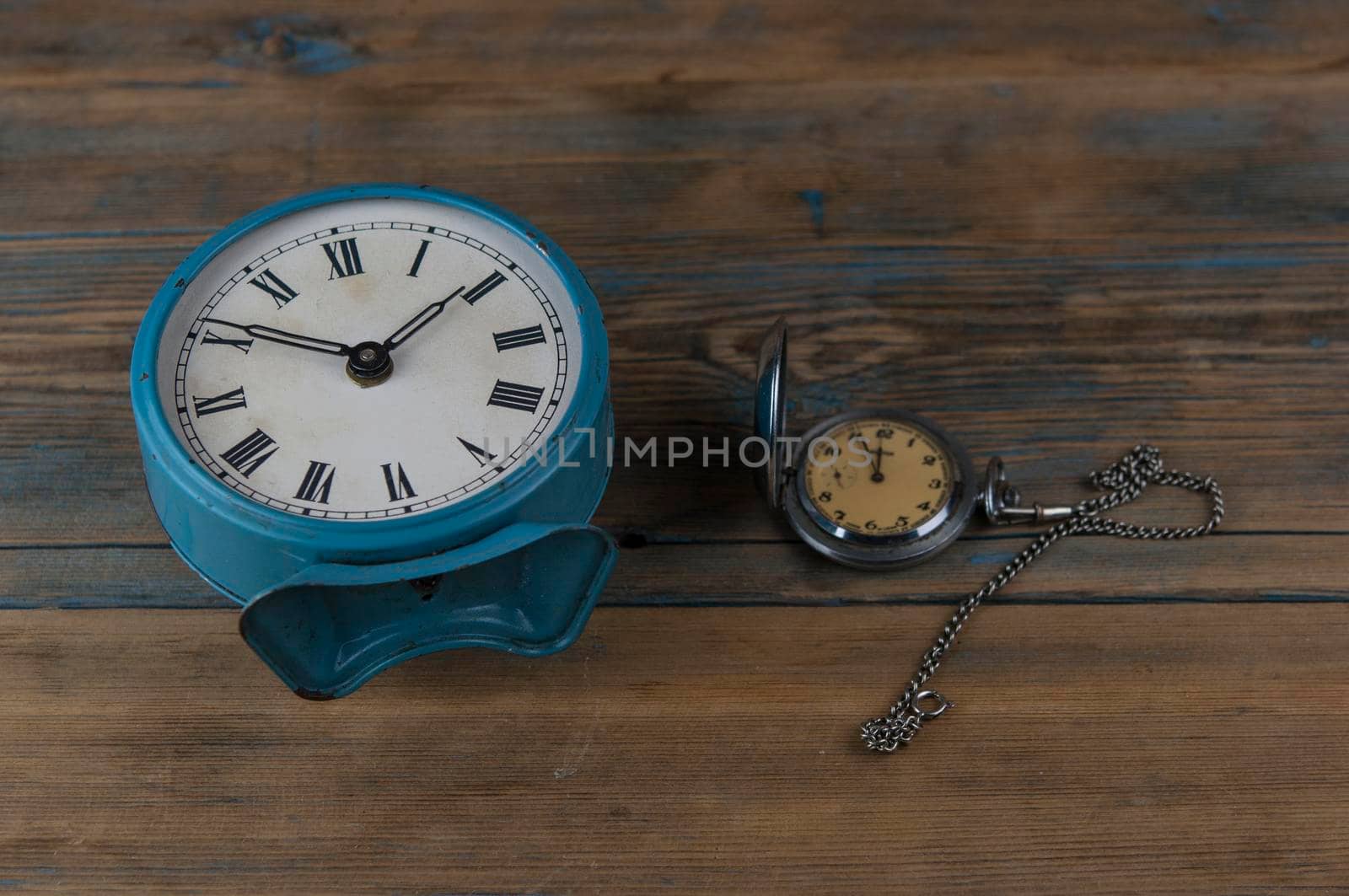 Alarm clock with roman numerals and vintage pocket watch on wooden table by inxti