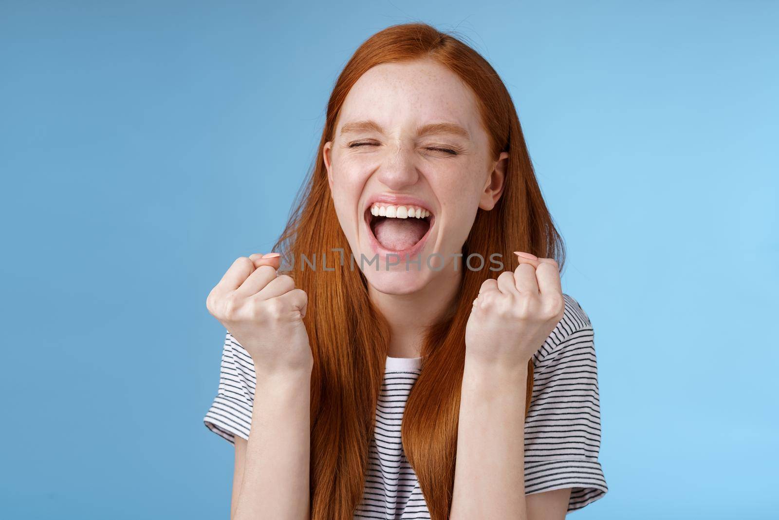 Yes achievement goal lifetime. Smiling happy european redhead girl raising clenched fists cheerful rejoicing yelling yeah accomplish goal success triumphing victory, great news win lottery by Benzoix