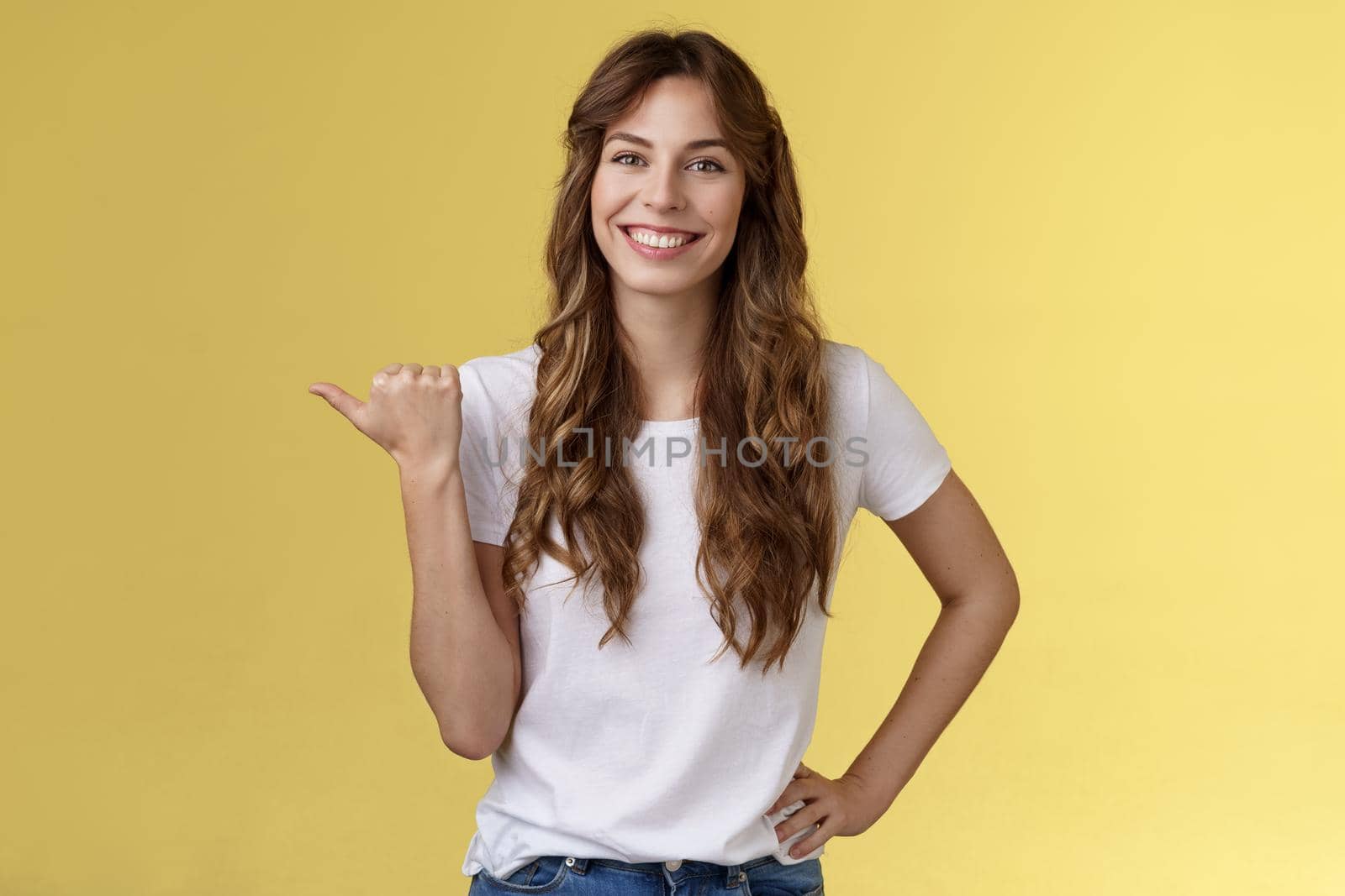 Friendly outgoing cheerful european cute female giving tips showing direction lively smiling toothy happily have nice pleasant conversation pointing left thumb introduce promo yellow background by Benzoix