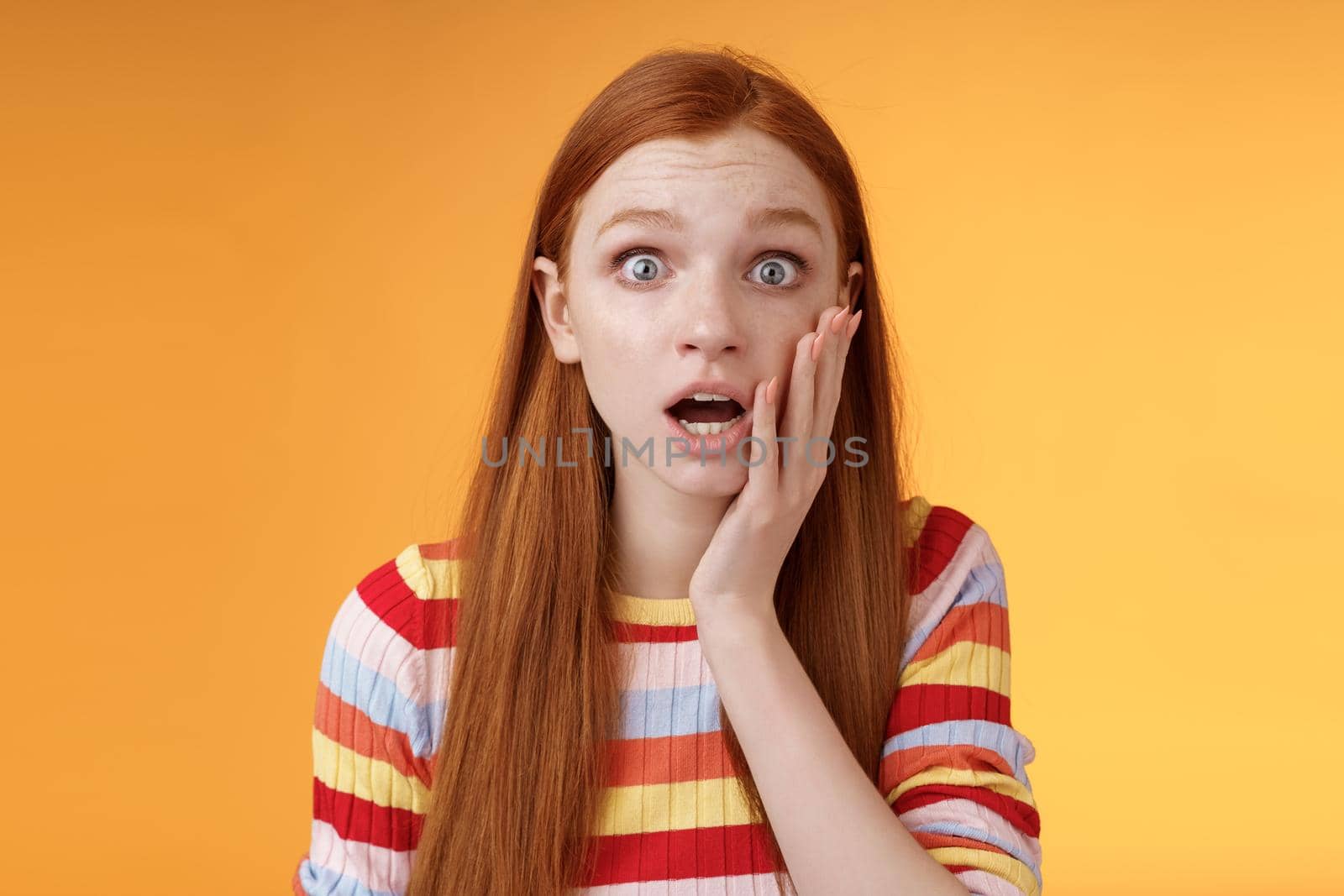 Concerned worried ginger girl blue eyes drop jaw gasping touch cheek confused looking nervously anxious, show empathy hearing terrible upsetting story standing orange background by Benzoix