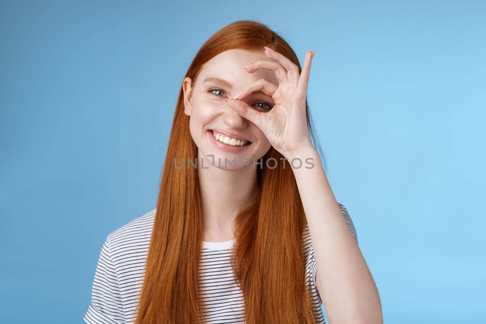 Charismatic happy adorable redhead teenage girl sincere eyes making circle eye show okay ok sign delighted like approve cool idea smiling satisfied achieve perfect score, standing blue background by Benzoix