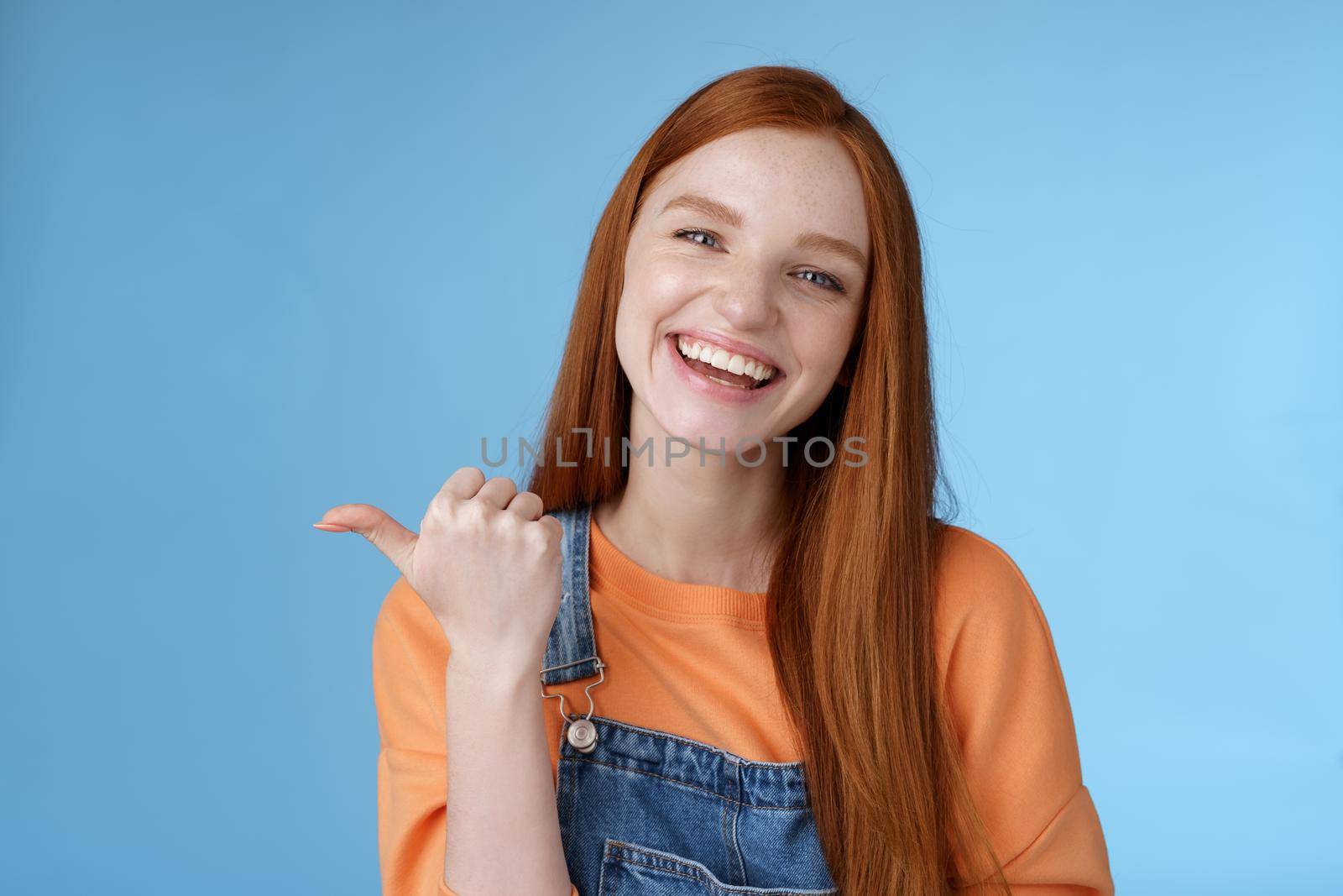 Girl introducing her friend pointing thumb left smiling laughing joyfully proudly telling pros cool product recommend telling about cozy cafe tasty coffee having fun posing blue background by Benzoix
