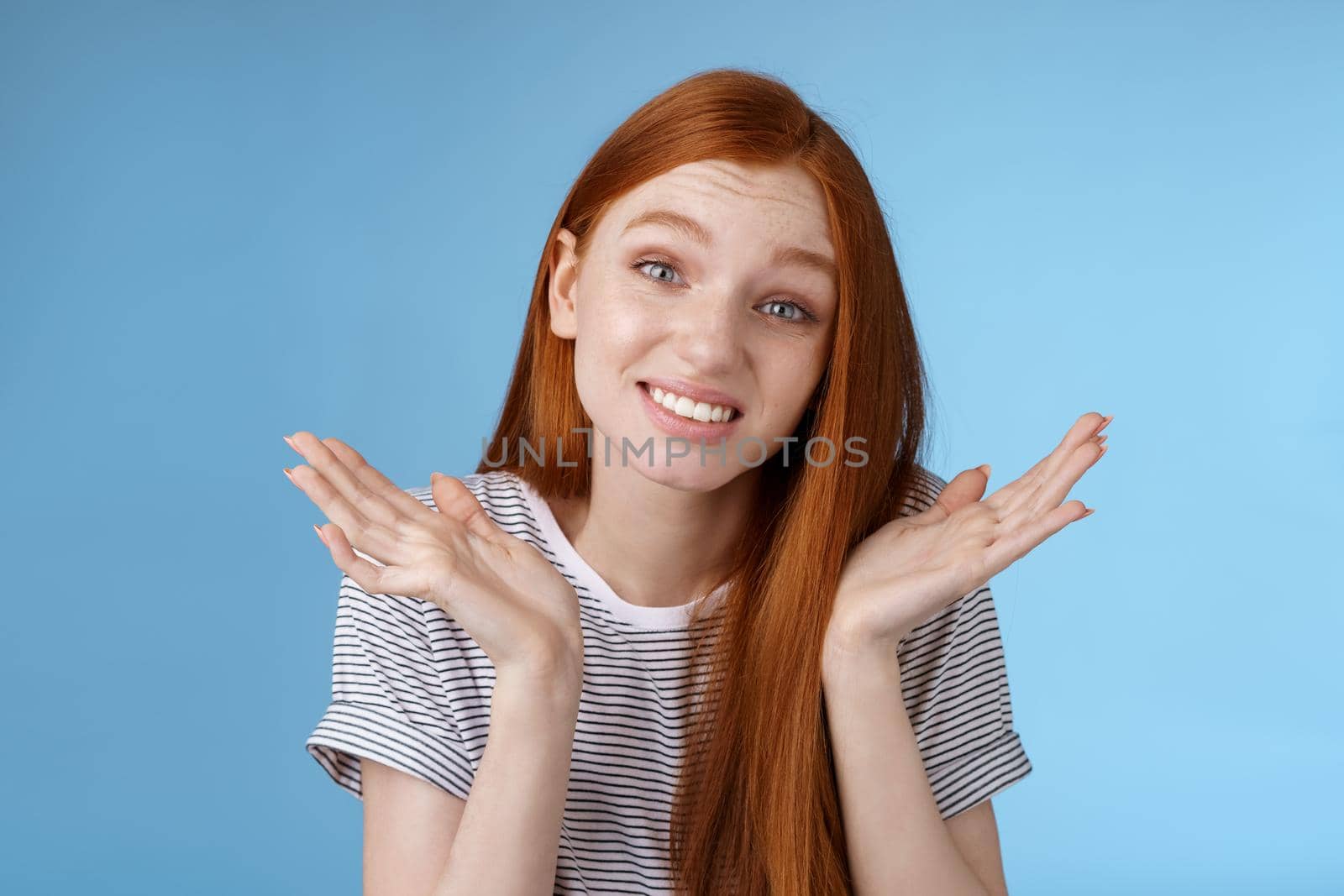 Awkward apologizing cute redhead girlfriend say sorry shrugging spread hands sideways puzzled smiling uncomfortably standing clueless unaware forgetting meeting, posing blue background by Benzoix