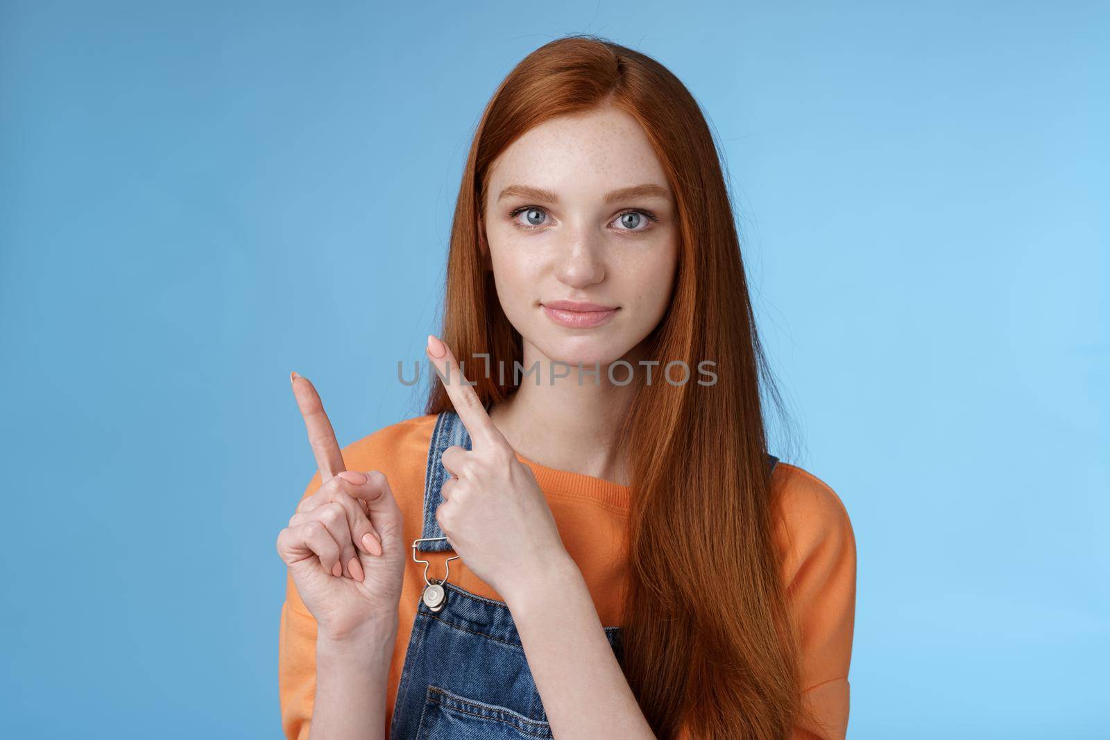 Assertive good-looking redhead girl know what talking about pointing upper left corner index fingers showing confidently good product recommend check out standing blue background by Benzoix