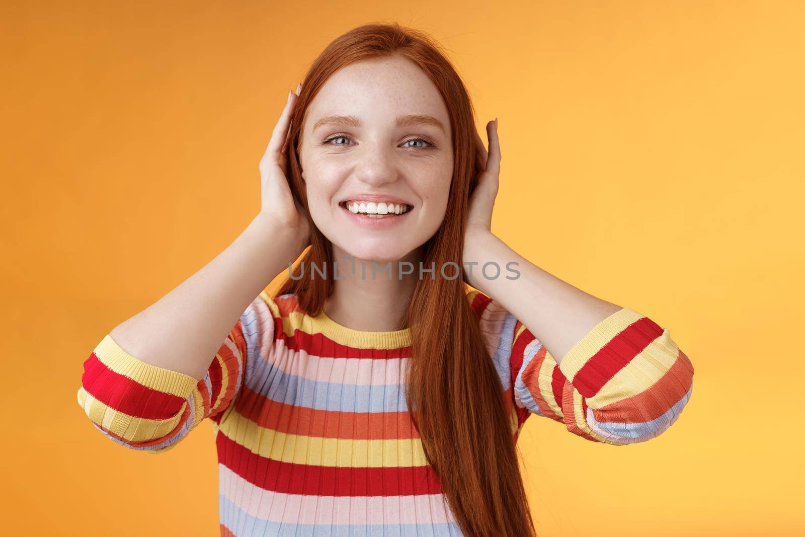 Cute playful tender smiling ginger girl blue eyes silly cover ears palms grinning fool around not hear anyone carefree unwilling listen noisy people standing careless relaxed orange background by Benzoix