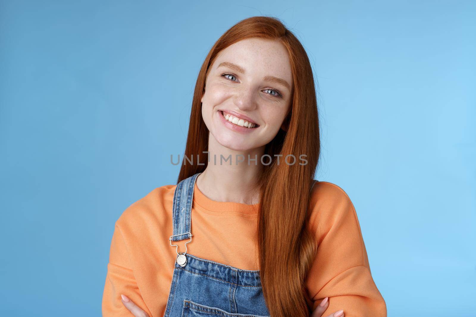 Charismatic kind pleasant redhead girl blue eyes smiling friendly listen politely customer standing blue background tilting head amused grinning cross hands chest professional confidence pose by Benzoix