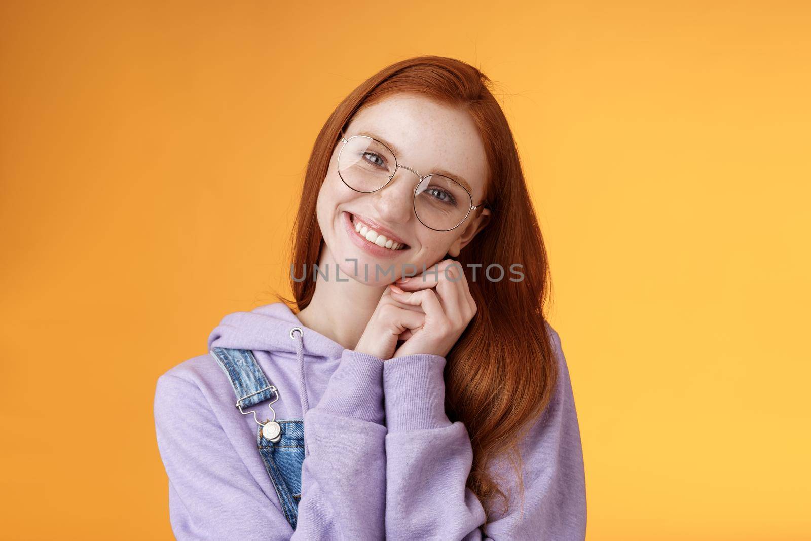 Tender feminine ginger girl blue eyes wearing glasses hoodie lean palms smiling receive sweet cute gift think you lovely grateful dearest friend grinning joyful spread love, orange background.