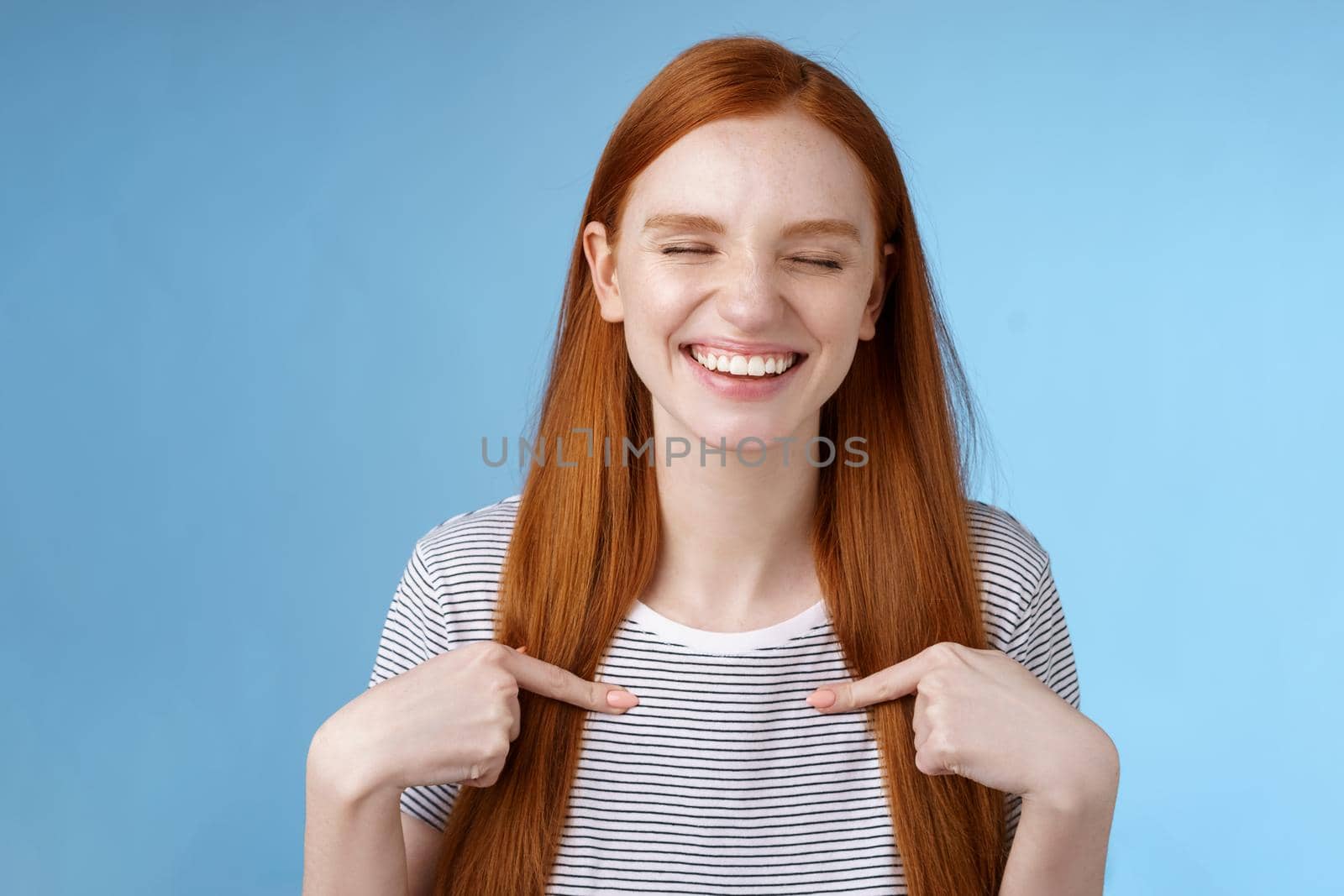 Happy cheerful glad young sportswoman redhead nominated smiling surprised laughing joyfully close eyes pointing herself chosen picked winning first prize, standing blue background by Benzoix