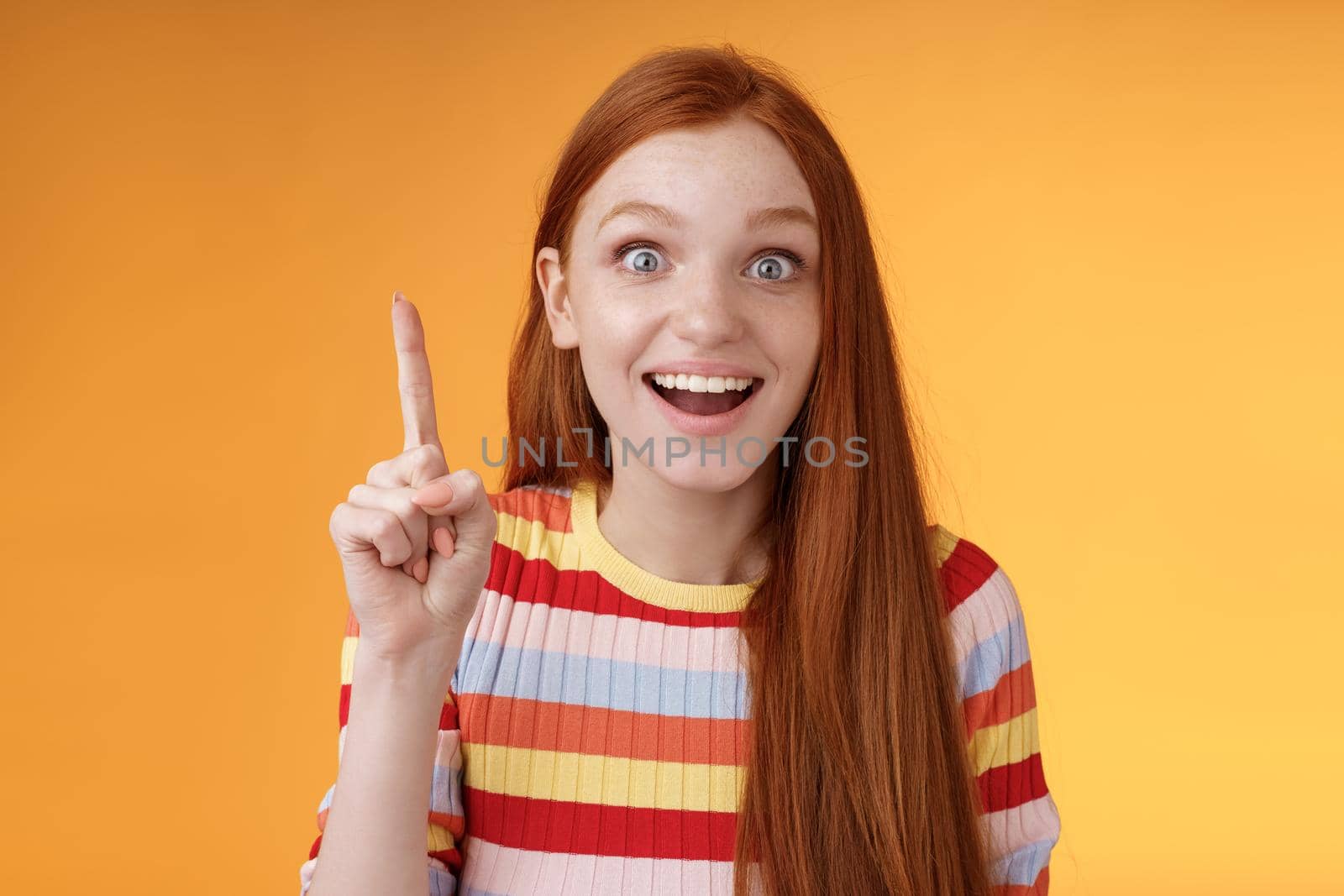Excited happy cheerful young redhead female student got idea think answer raising index finger eureka gesture smiling thrilled wide eyes saying plan have excellent suggestion, orange background by Benzoix