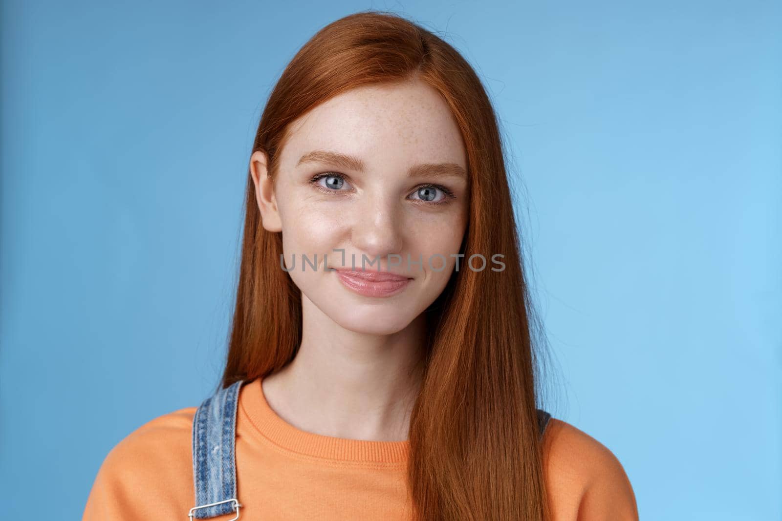 Outgoing young redhead girl blue eyes wearing orange t-shirt overalls smiling pleasantly casually talking standing good mood joyful emotions blue background, listening interesting conversation by Benzoix