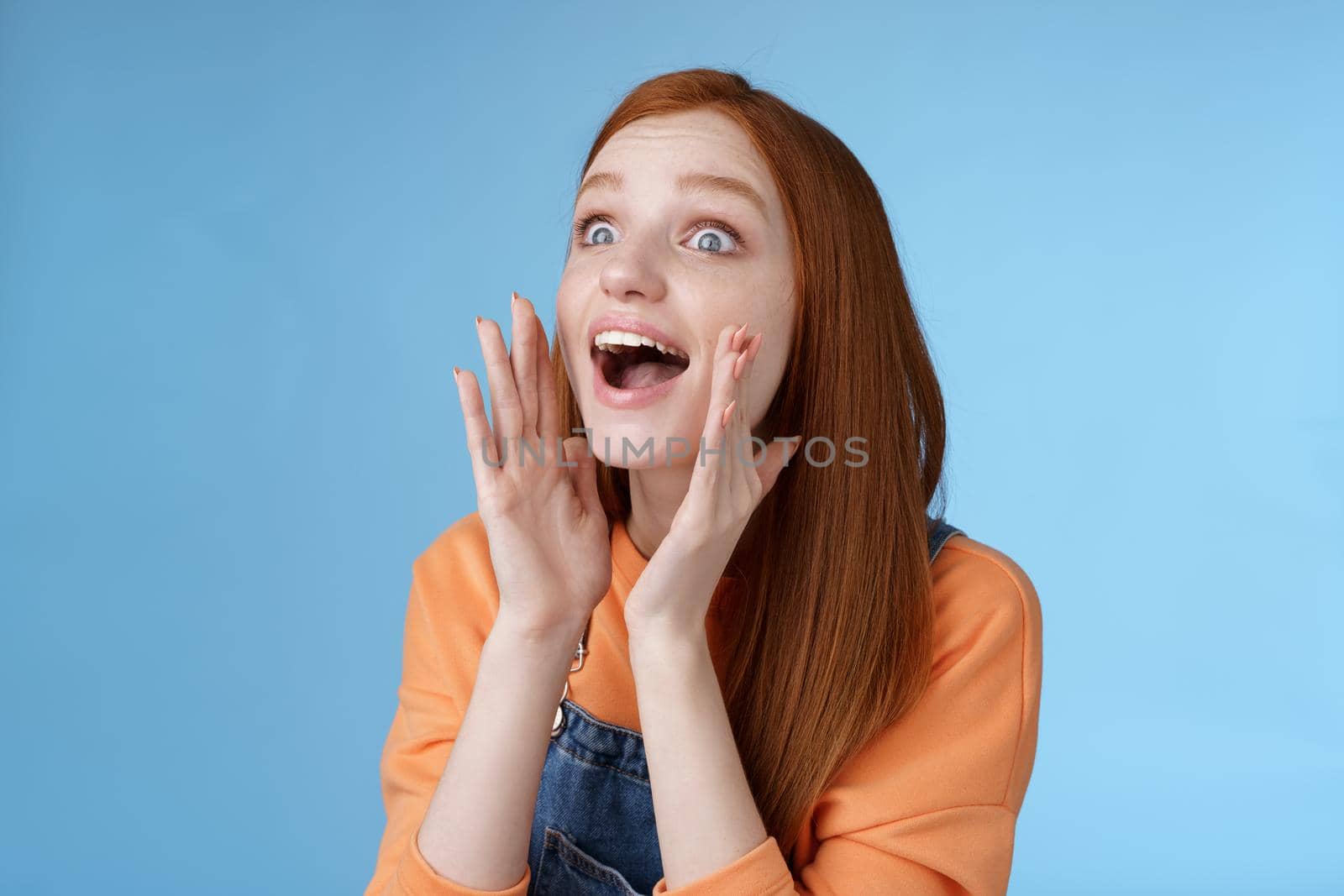 Attractive silly european redhead young girl 20s calling friend searching someone crowd look relaxed joyfully yelling hold hands opened mouth shouting name louder look left, blue background by Benzoix