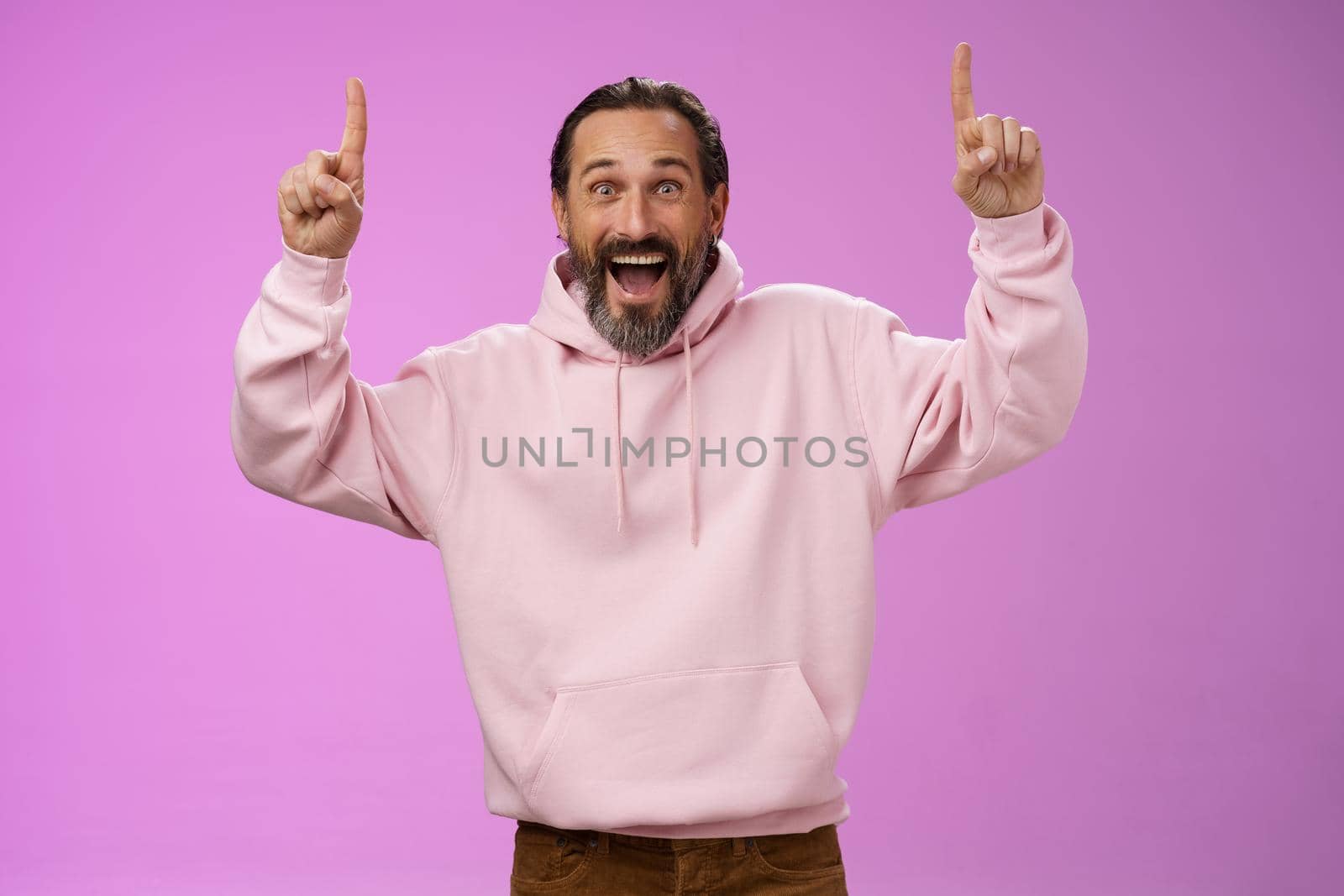 Energized happy good-looking trendy mature dad beard grey hair in pink stylish hoodie wearing son outfit pointing up index fingers thrilled favorite music group in town, standing purple background by Benzoix