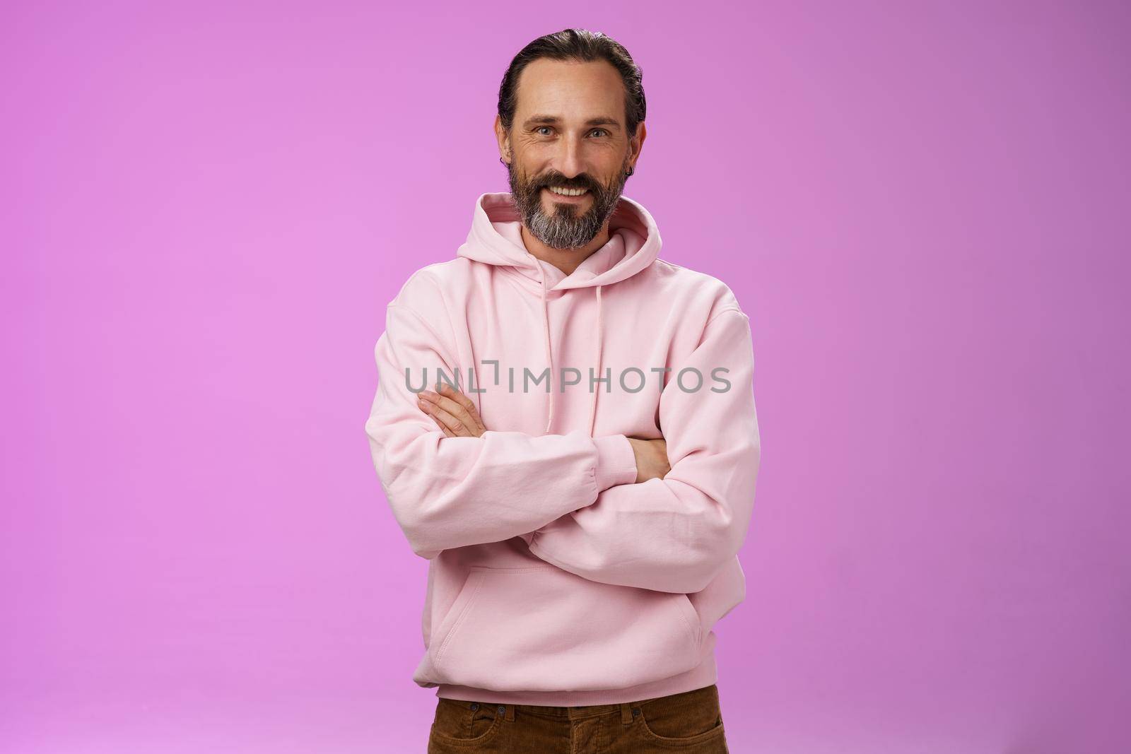 Portrait cool bearded mature grandad trying stay stylish urban trends wear pink hoodie cross arms chest casual pose smiling happily talking have conversation, posing purple background.