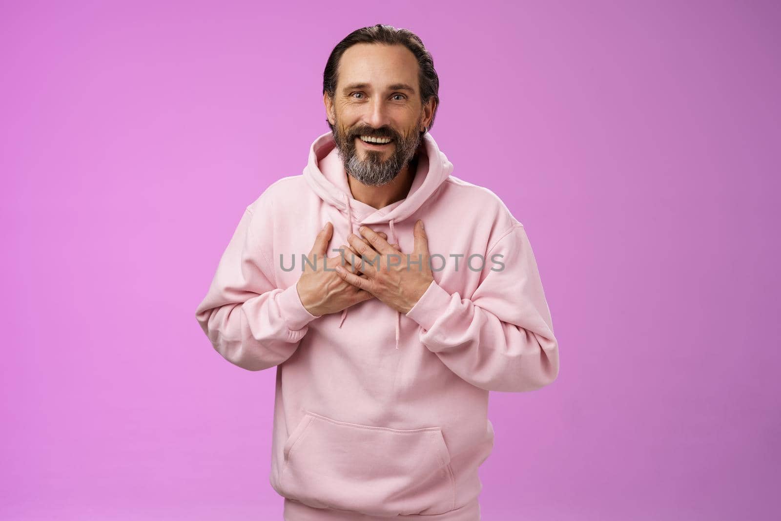 Thankful charming lucky adult bearded man 50s grey hair press palms heart receiving touching heartwarming gesture smiling grateful appreciating effort cherish moment, standing purple background.