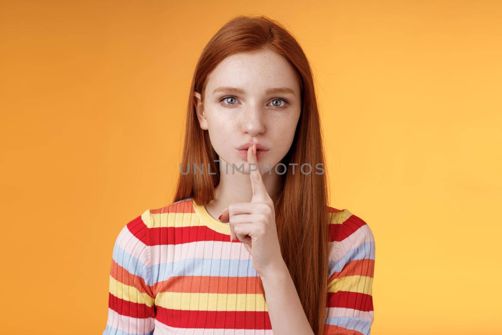 Girl hides lots secrets. Serious-looking redhead girlfriend blue eyes demand keep silent voice down show shhh shush gesture index finger pressed lips, prepare surprise, orange background.