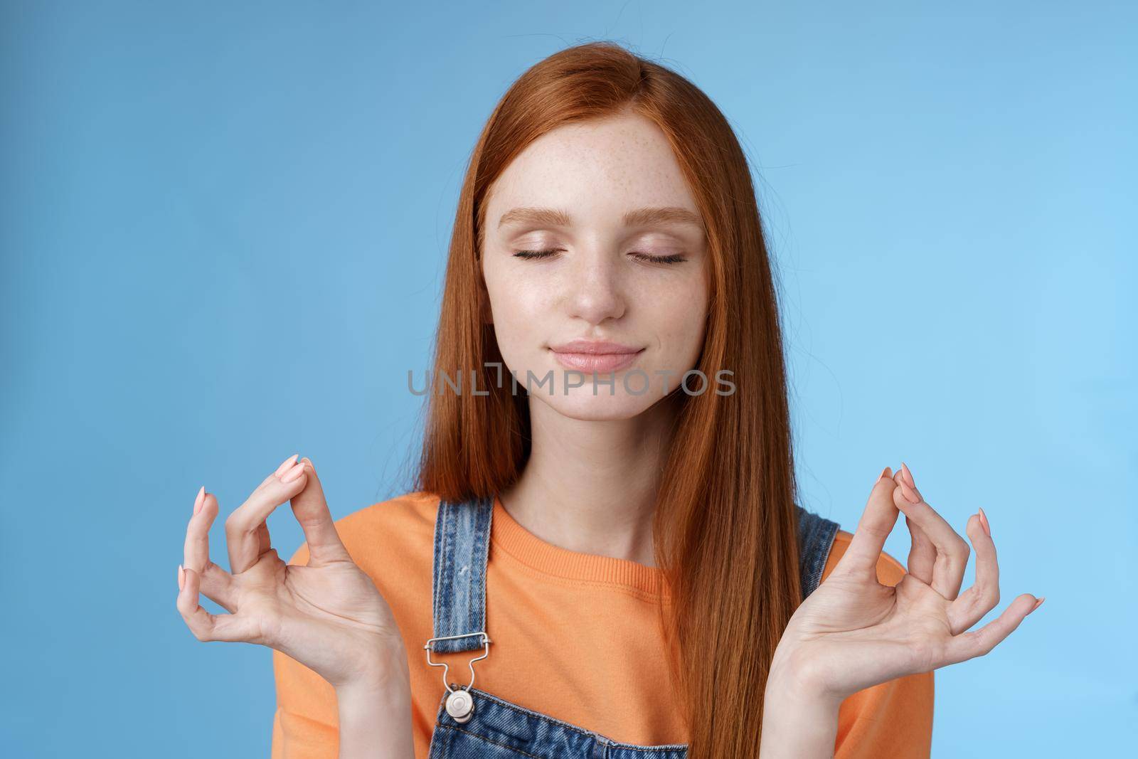 Keep calm redhead relaxed girl stay relieved positive close eyes smiling delighted raising hands sideways lotus mudra gesture practice yoga meditation do breathing exercise, blue background.