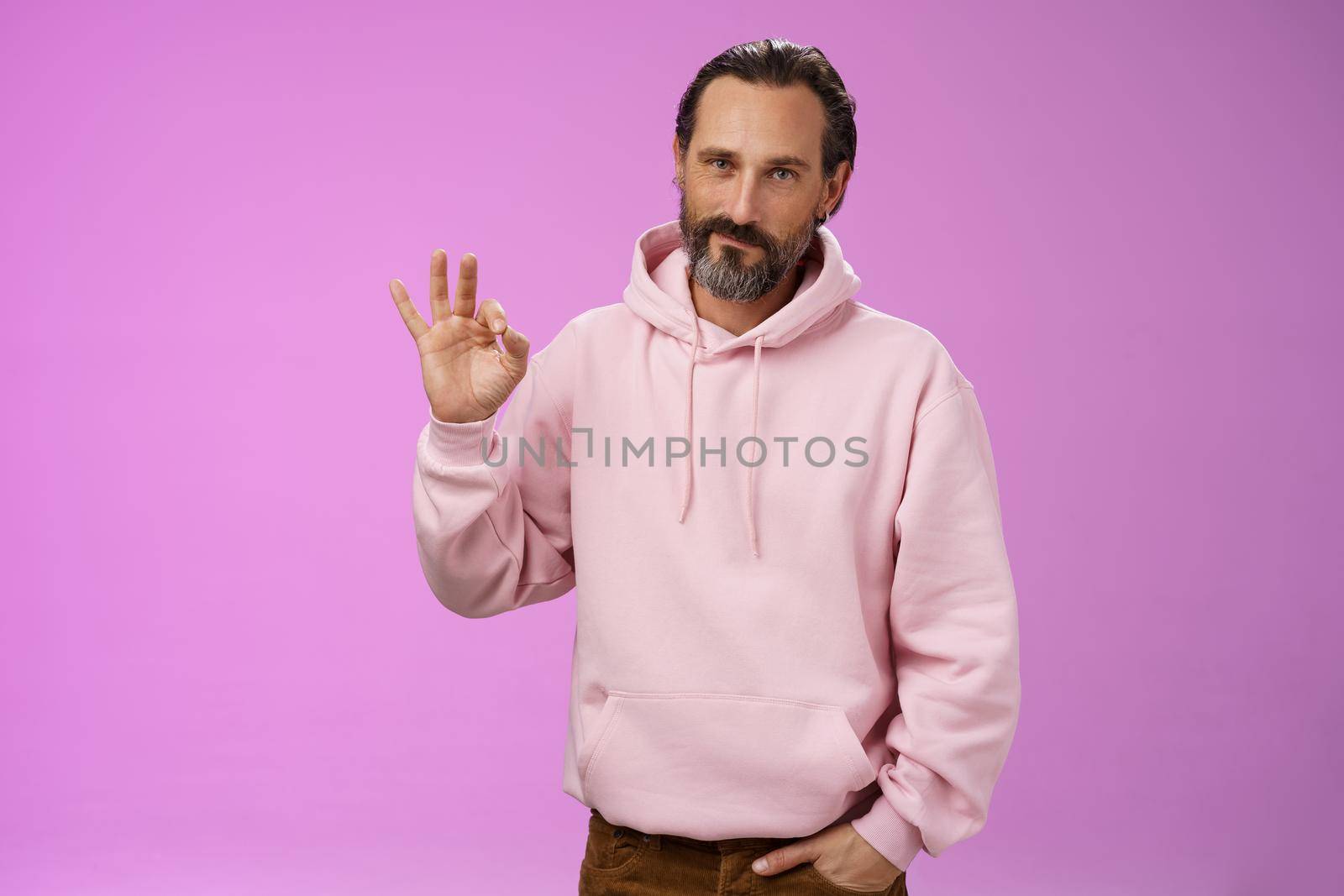 Confident good-looking lucky old macho guy bearded grey hair in stylish pink hoodie hold hand pocket show okay ok approval gesture smirking delighted agree daughter choice, posing supportive.