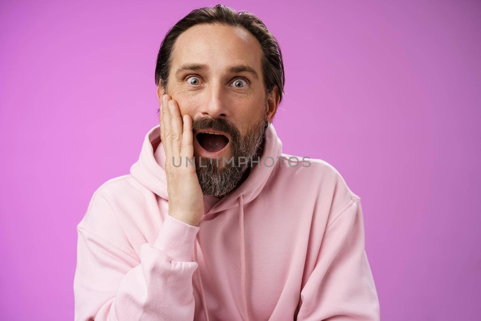 Impressed fascinated speechless mature male attend interesting lecture drop jaw thrilled touch cheek palm widen eyes surpised astonished, standing purple background amzed and amused by Benzoix