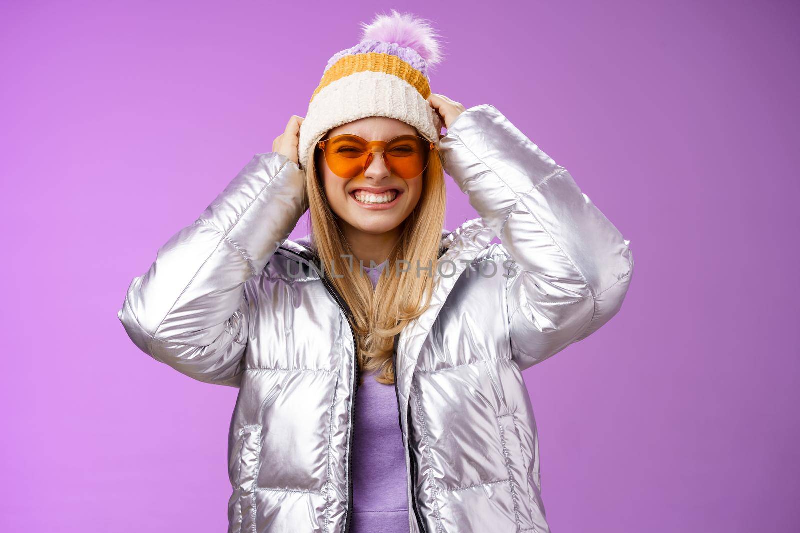 Energized daring sassy young attractive woman having fun friends winter trip learn snowboarding smiling cheeky enjoying vacation put-on hat wearing silver warm jacket sunglasses, purple background by Benzoix