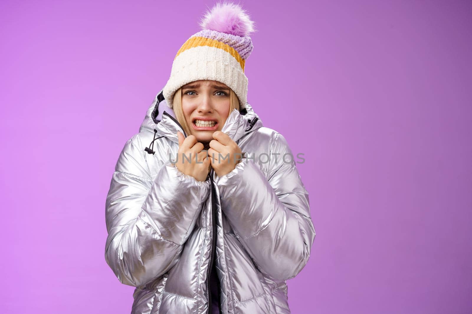 Lifestyle. Uncomfortable shaking displeased charming gloomy blond cute woman in silver stylish jacket pulling coat tight wear hat shaking clenching teeth grimacing suffering low temperature freezing cold.