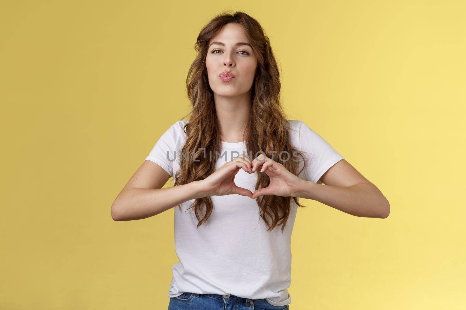 Passionate sensual attractive girlfriend express love sympathy show heart sign near chest folding lips kiss sending muah camera look admiration confess deep romantic feelings adore you by Benzoix