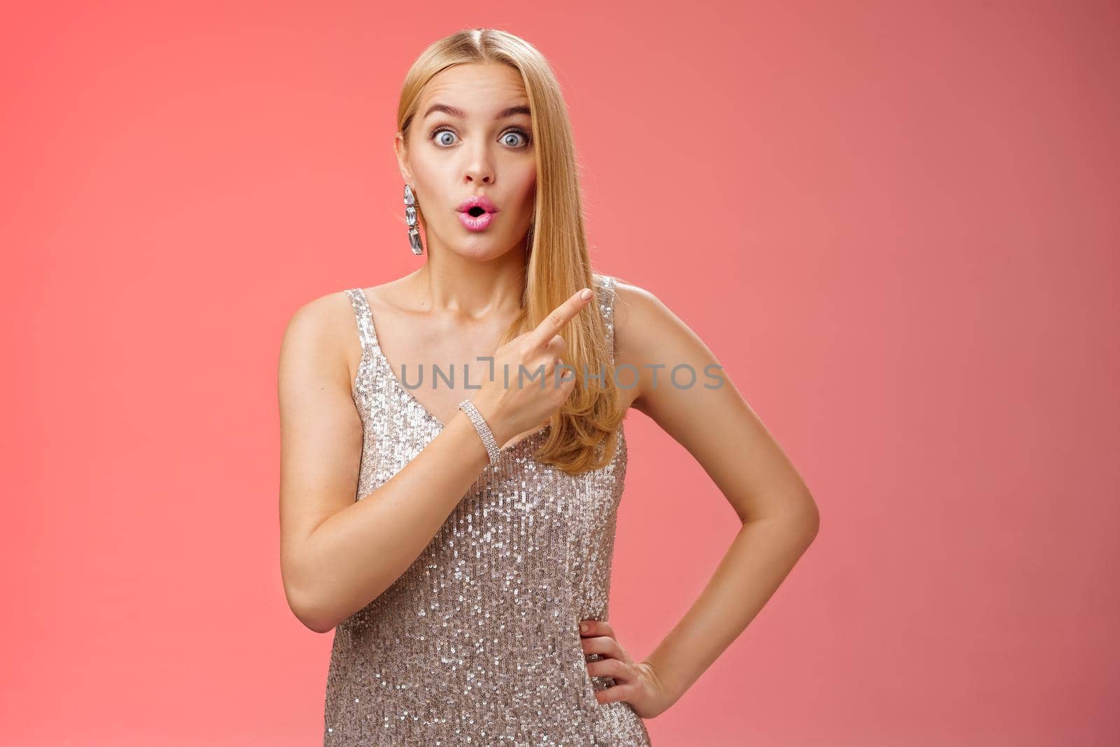 Wondered amused attractive blond woman talking party widen eyes say wow pointing questioned right direction see famous person standing surprised impressed gaze camera, red background by Benzoix