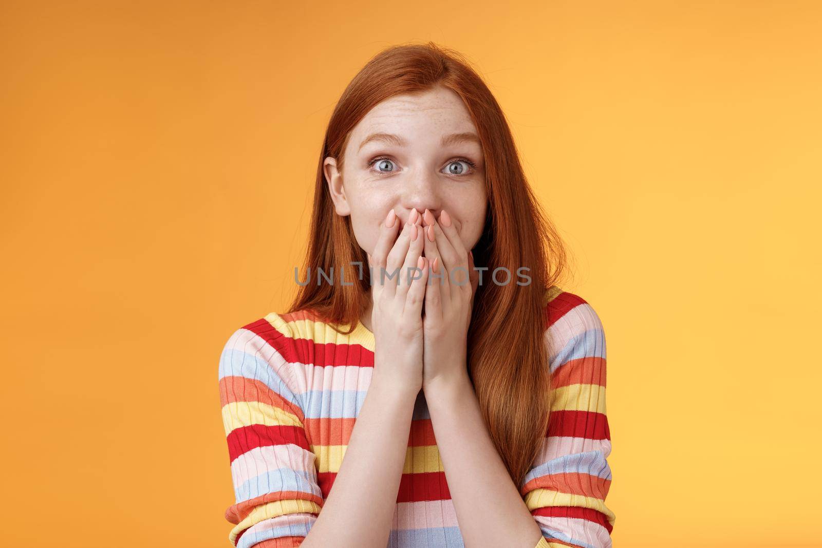 Shocked surprised attractive cute redhead girl receive awesome chance smiling impressed gasping cover mouth palms wide eyes excited happily reacting incredible good news, standing orange background by Benzoix