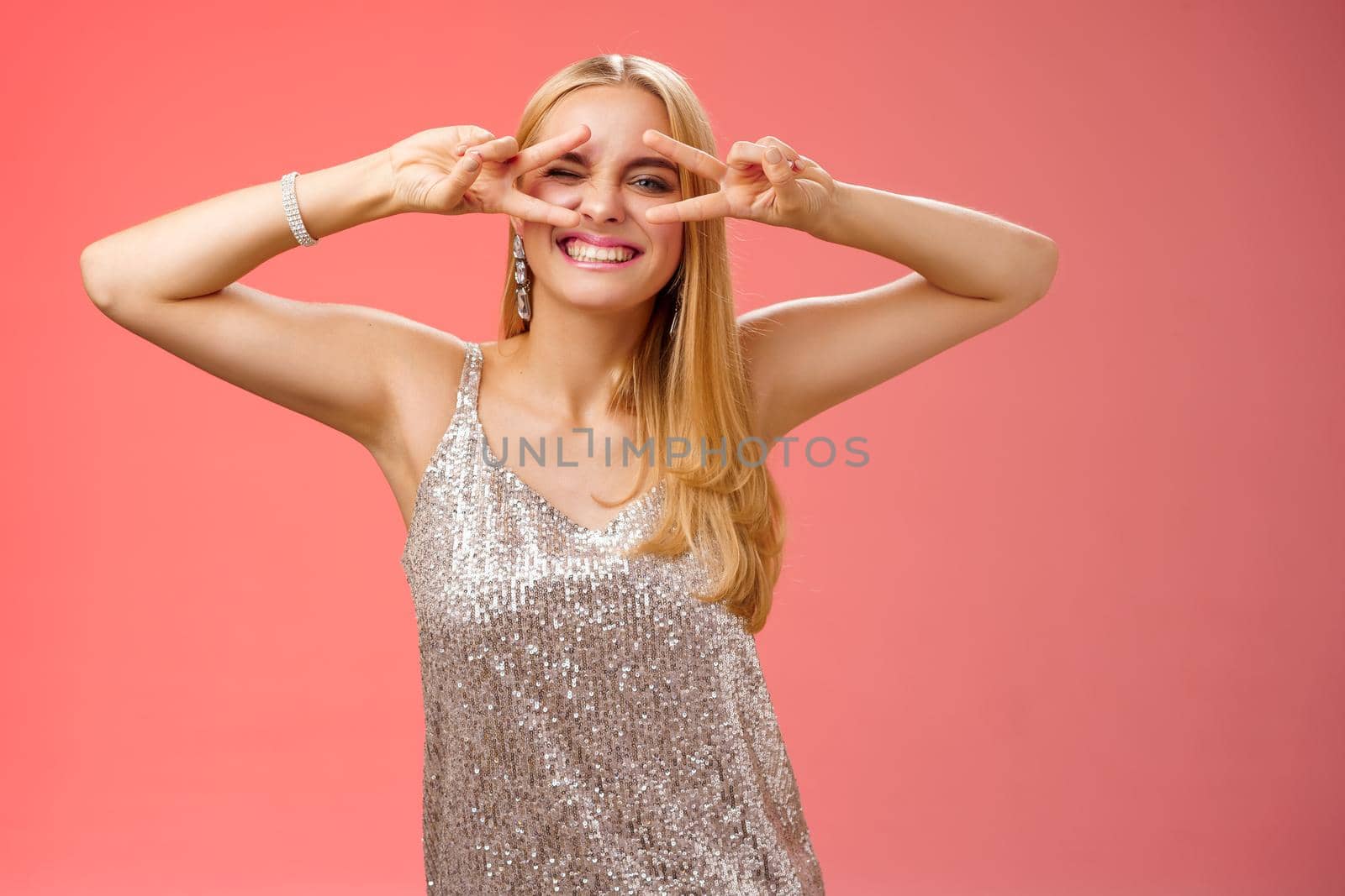 Sassy attractive stylish european girlfriend having fun celebrating birthday standing silver evening glittering dress winking cheeky make disco peace gesture near eyes enjoying party, red background.