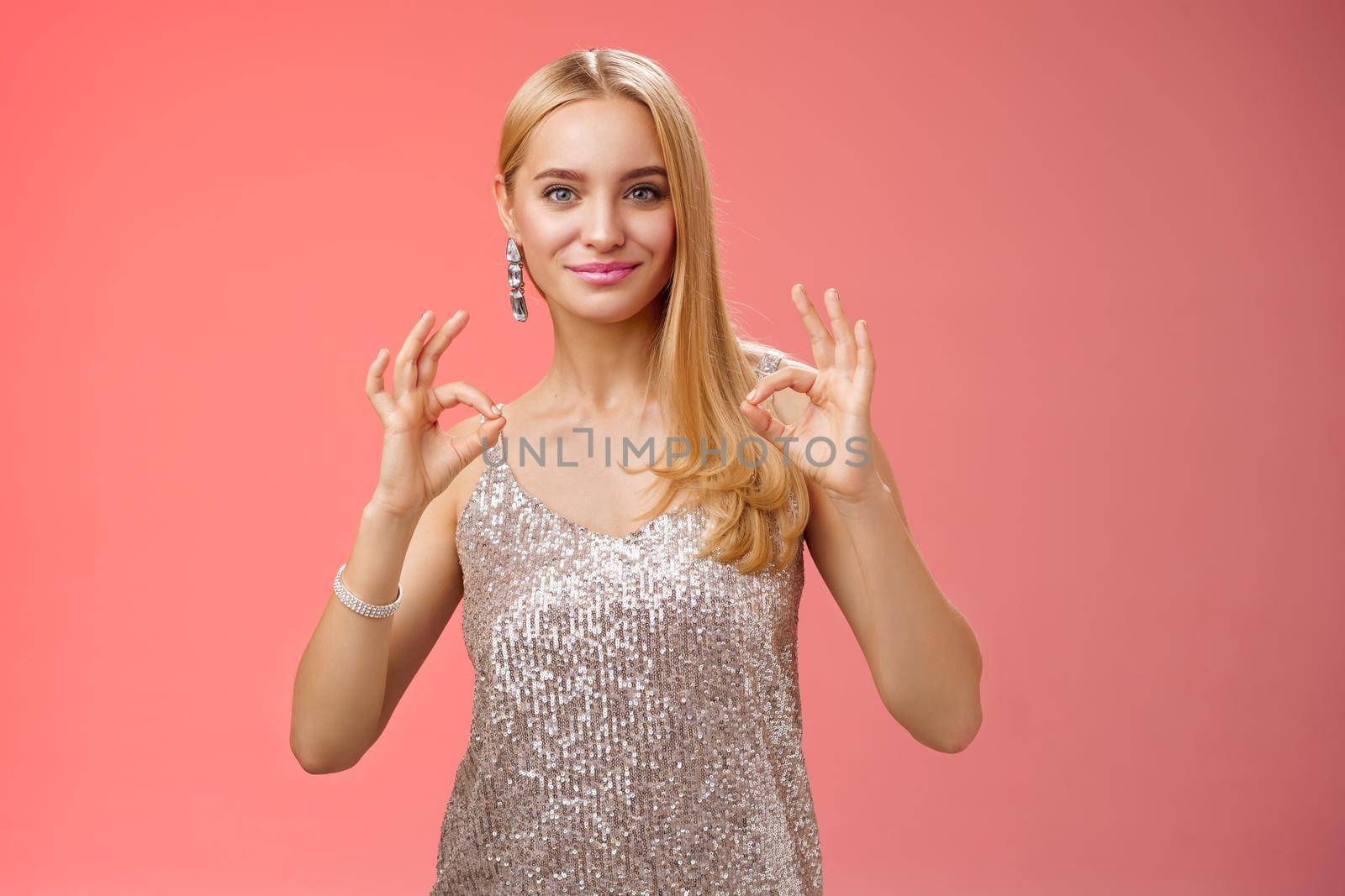 Confident carefree optimistic young blond woman assure everything done perfect liking result show okay ok no problem gesture smiling self-assured standing silver luxurious dress, red background.