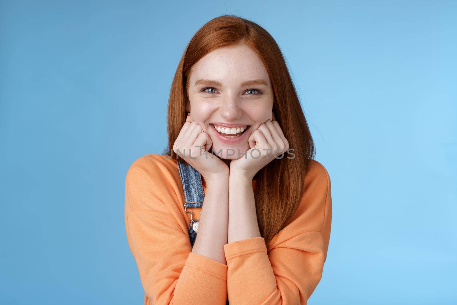 Enthusiastic sassy good-looking redhead caucasian girl lean head palms look amused intrigued listen interesting story pleased smiling laughing silly jokes standing blue background excited happy by Benzoix