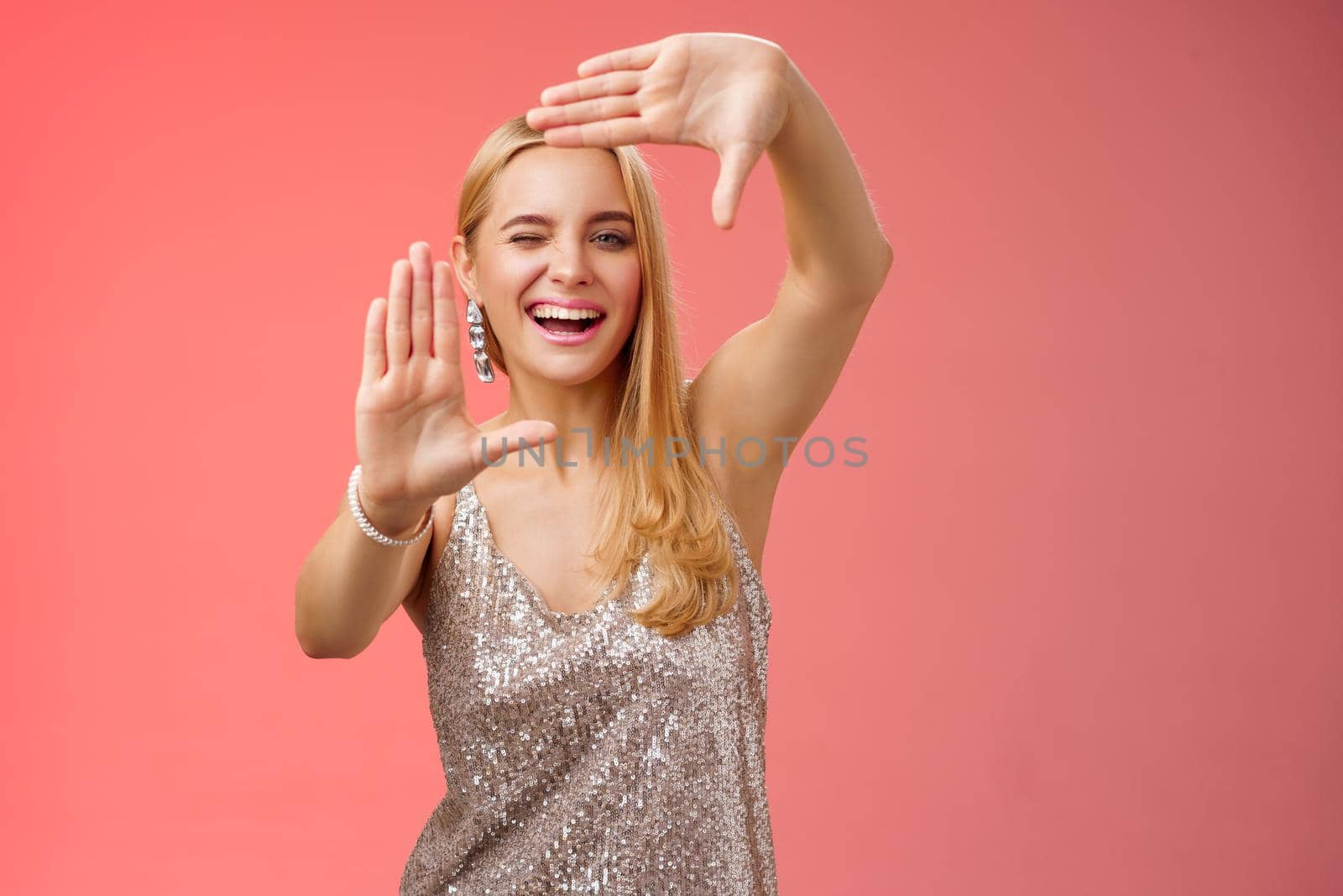 Sassy good-looking creative european blond woman in silver glittering dress winking cheeky smiling confident search inspiration around make frame hand search location take cool shot, red background by Benzoix