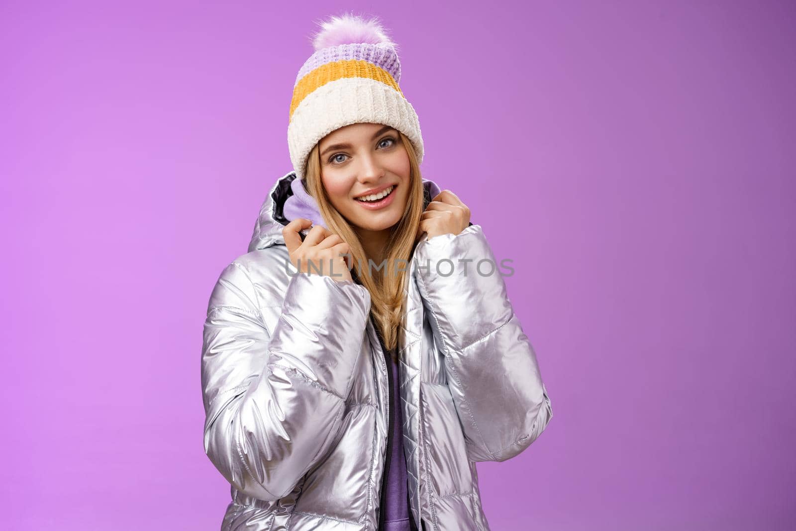 Tender feminine gentle blond girlfriend posing boyfriend take pictures ski resort holiday wearing glittering stylish jacket winter hat standing pleased purple background smiling delighted by Benzoix