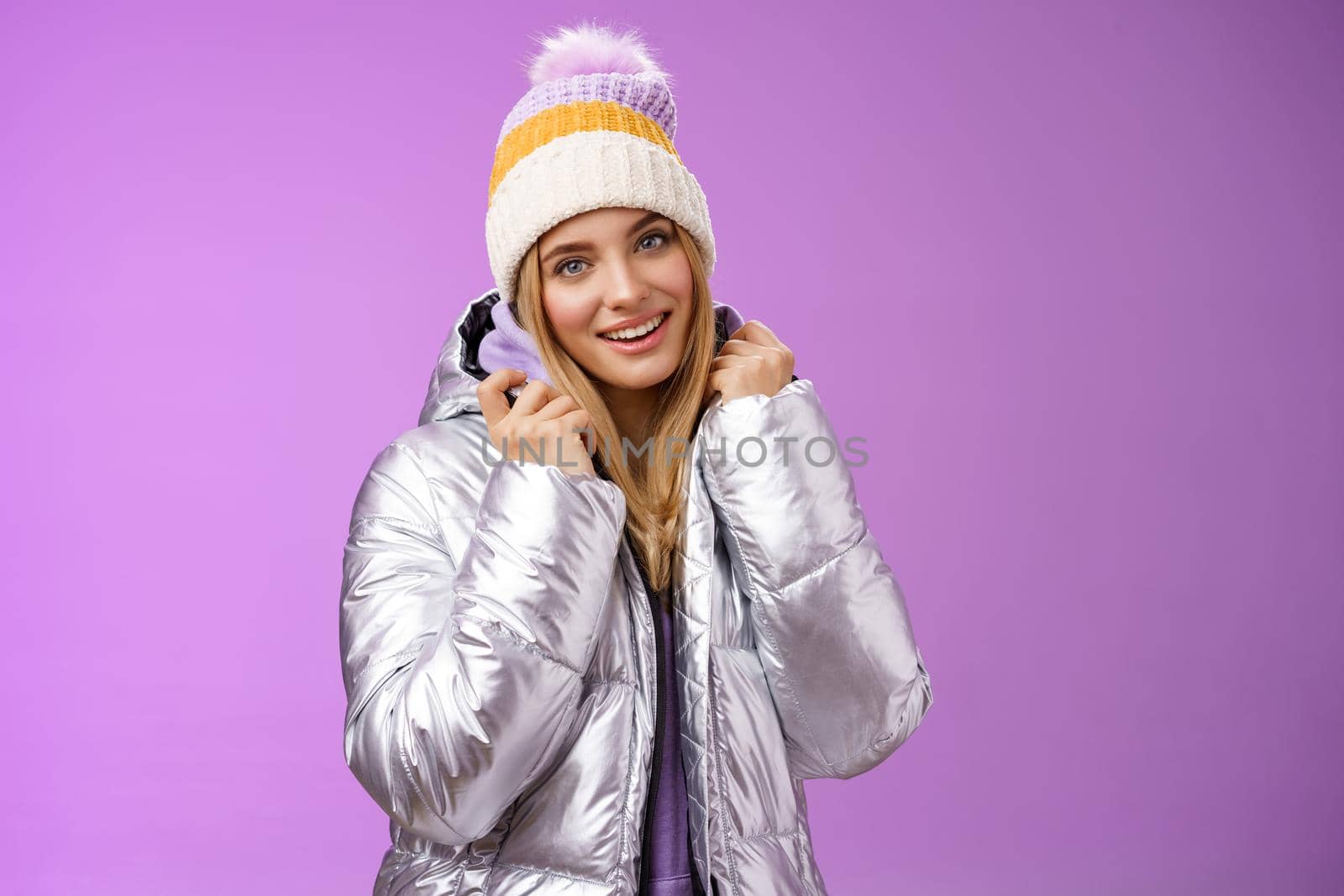 Tender feminine gentle blond girlfriend posing boyfriend take pictures ski resort holiday wearing glittering stylish jacket winter hat standing pleased purple background smiling delighted.