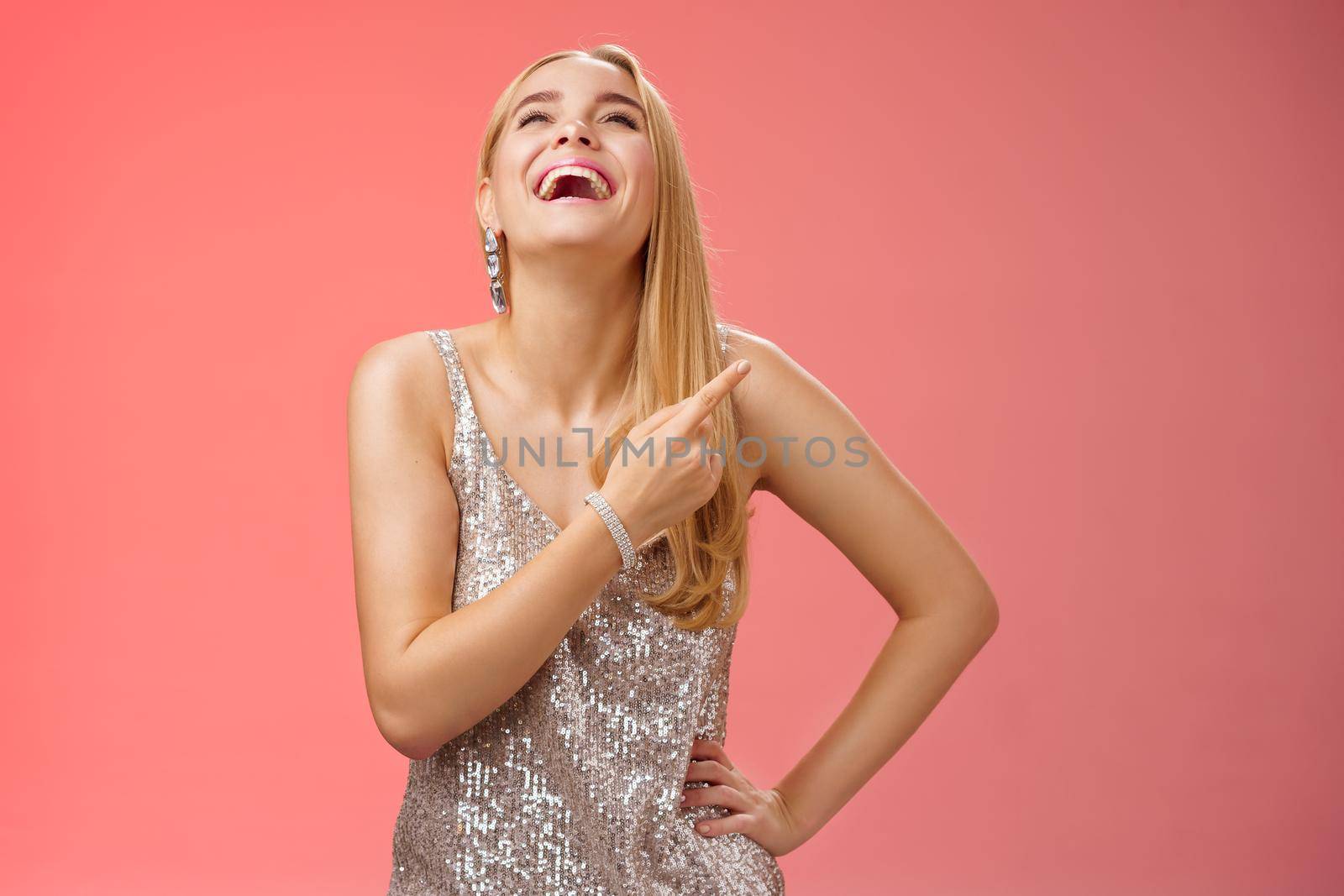 Fabulous carefree attractive blond woman in silver evening party dress laughing out loud have fun raise hand joyfully up pointing right index finger enjoying awesome sense humour, red background by Benzoix
