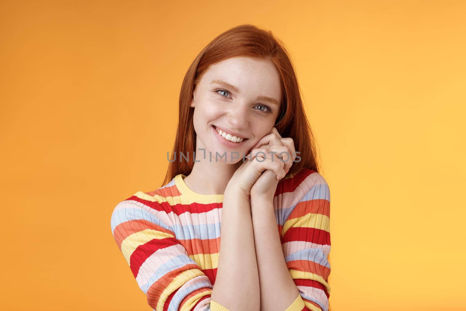 Romantic tender sensual attractive smiling redhead girlfriend melting heart feel warmth delighted lean palms grinning happily sweet gentle gift standing pleased orange background rejoicing thankful.