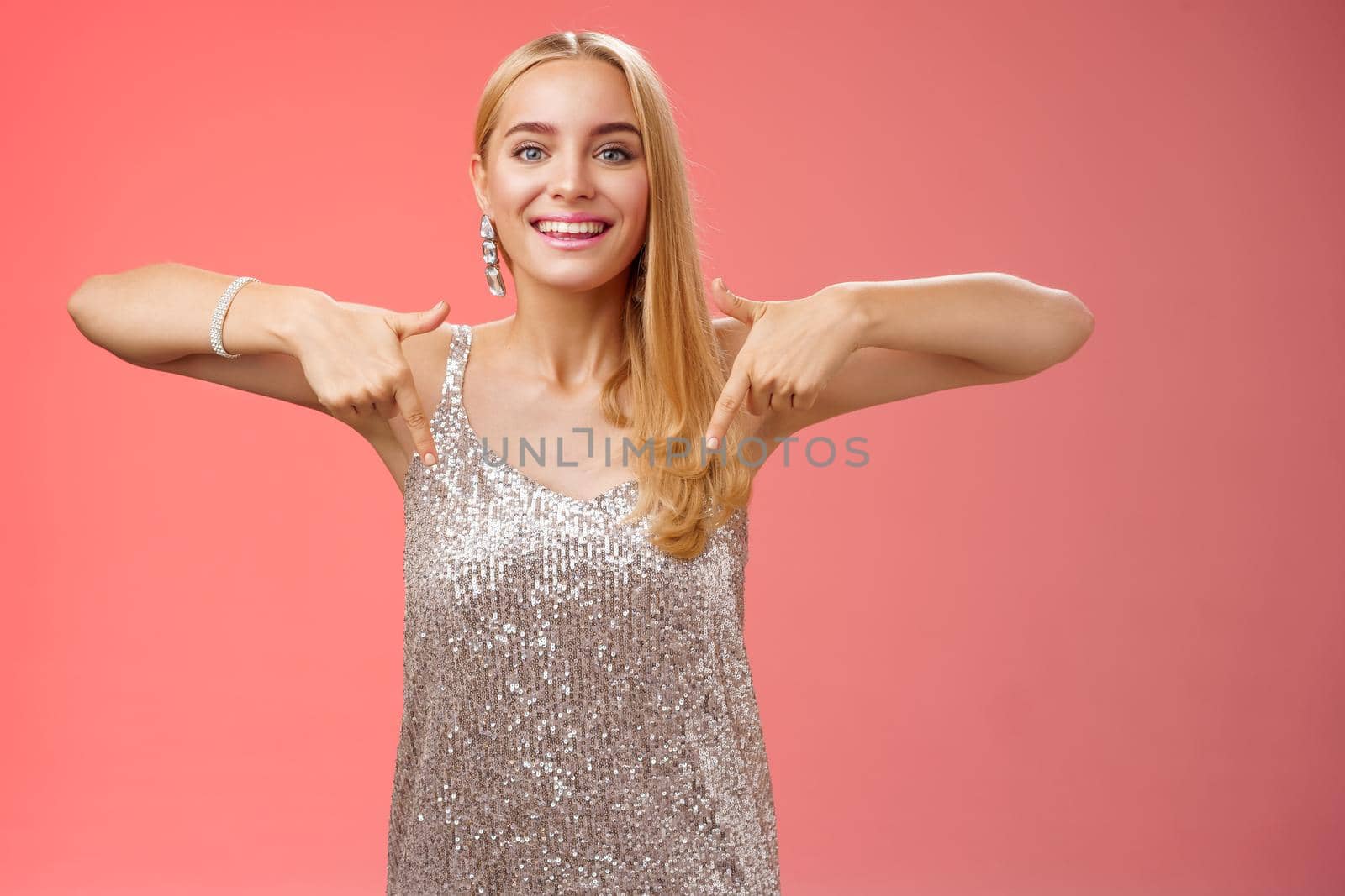 Attractive glamour blond woman in silver glittering dress pointing down smiling excited showing awesome party place hang-out inviting try-out standing pleased red background enjoying perfect evening by Benzoix