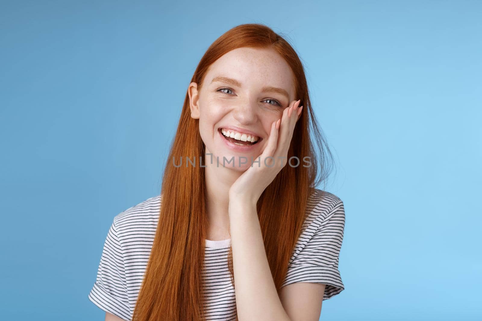 Charismatic talkative friendly-looking happy laughing redhead girl having fun discuss previous summer holidays make jokes chuckling touching face amused standing cheerful blue background by Benzoix