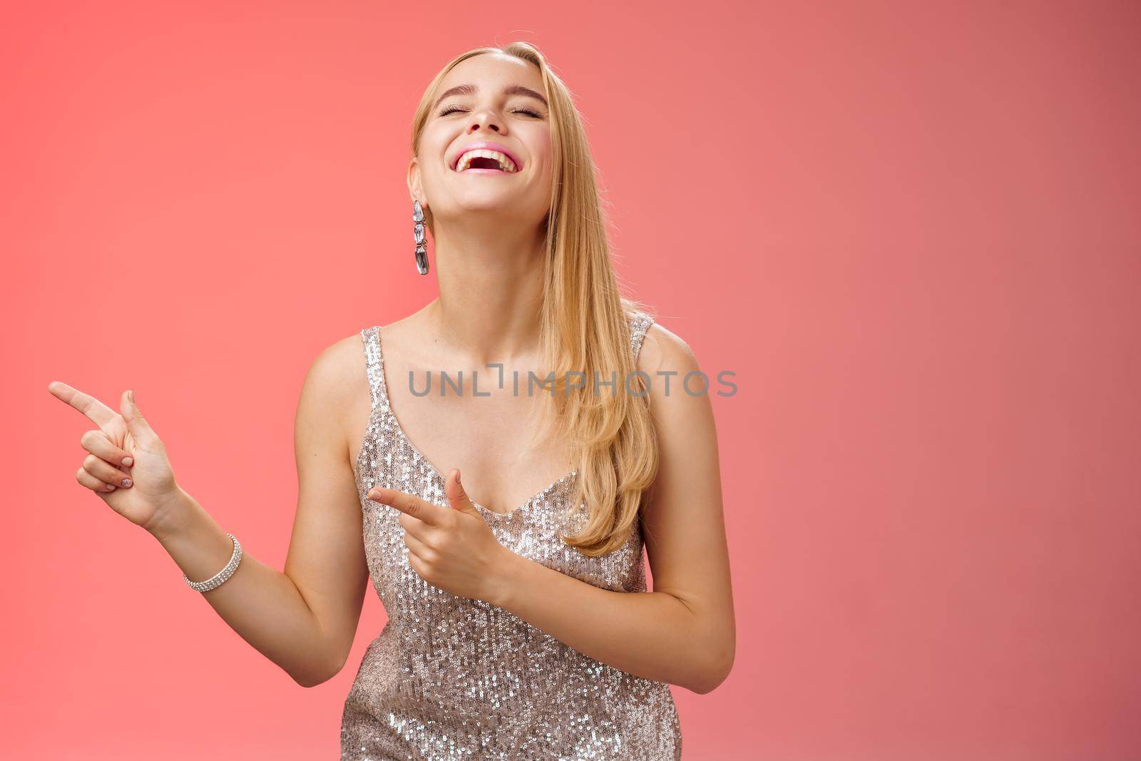 Funny carefree blond european woman in silver glittering evening dress raise head up close eyes laughing happily pointing left see hilarious person joking fool around, standing red background by Benzoix