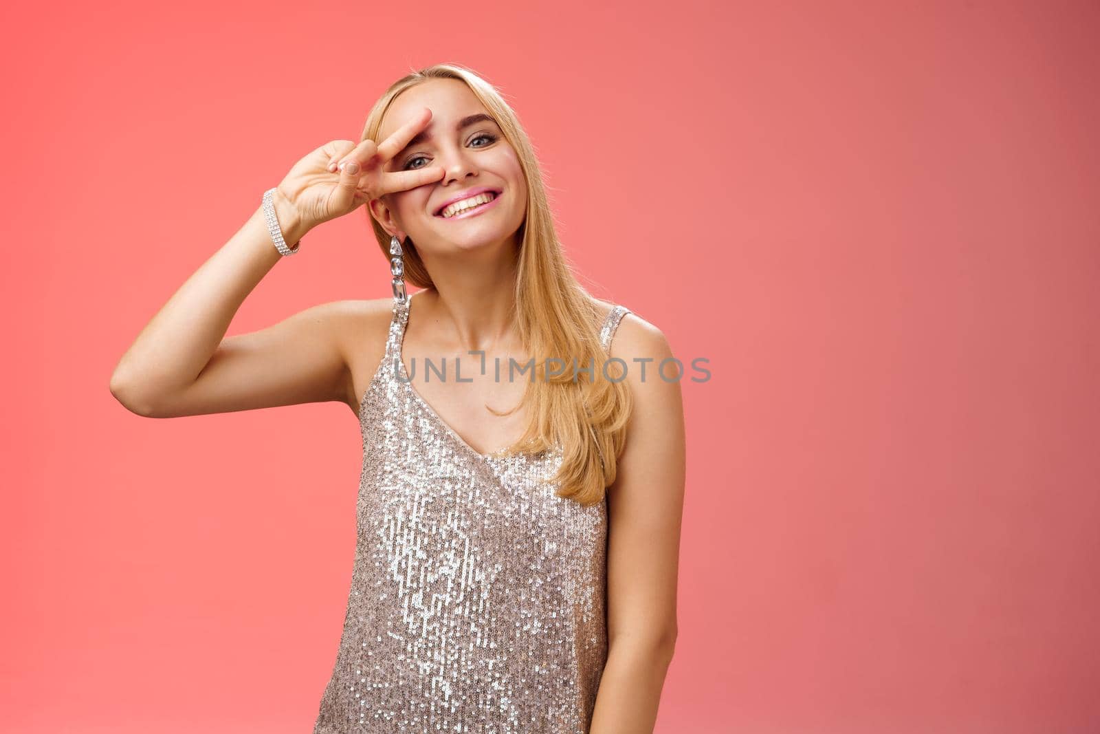 Optimistic lucky elegant european blond young 25s wife in silver glittering dress having fun enjoying celebration party dance floor showing peace victory sign eye smiling delighted, red background by Benzoix