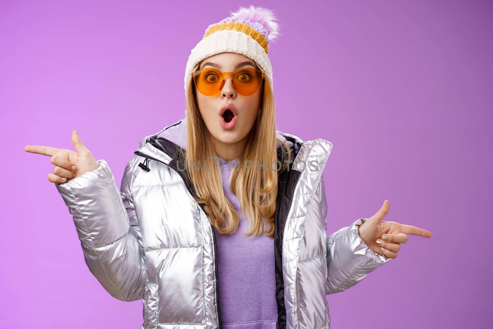 Impressed blond girl gasping widen eyes surprised folding lips wow sound check out incredible discounts winter equipment pointing left right cannot choose standing astonished purple background by Benzoix