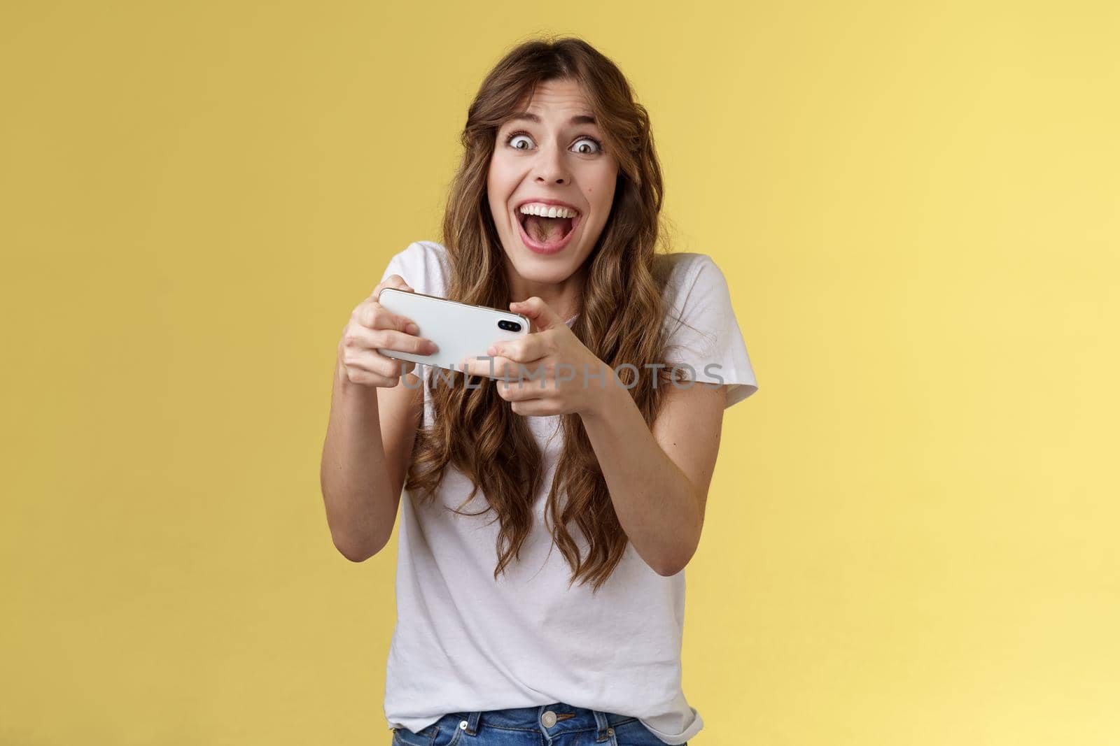 Extremely happy thrilled playful girl gamer playing awesome great new smartphone game hold mobile phone horizontal cheering look camera astonished impressed beating record yellow background by Benzoix