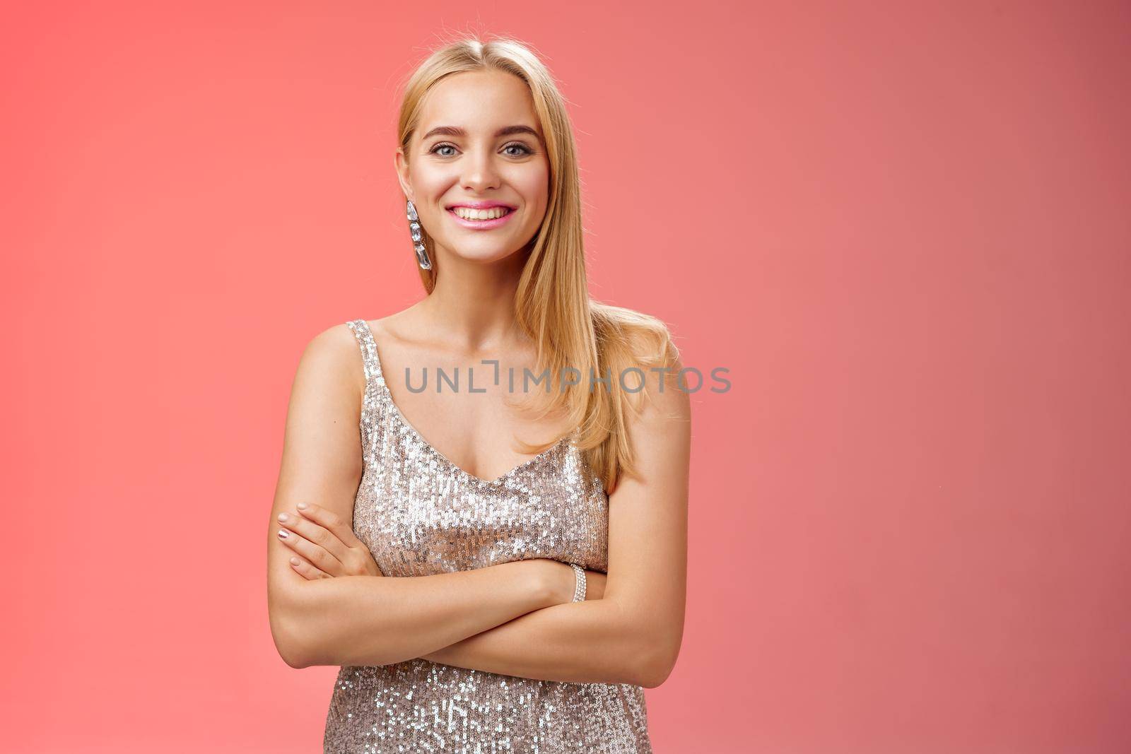 Charming tender blond girlfriend in silver shiny elegant dress feel little cold standing prom night talking boyfriend dance floor hold hand crossed chest grinning having fun, standing red background by Benzoix