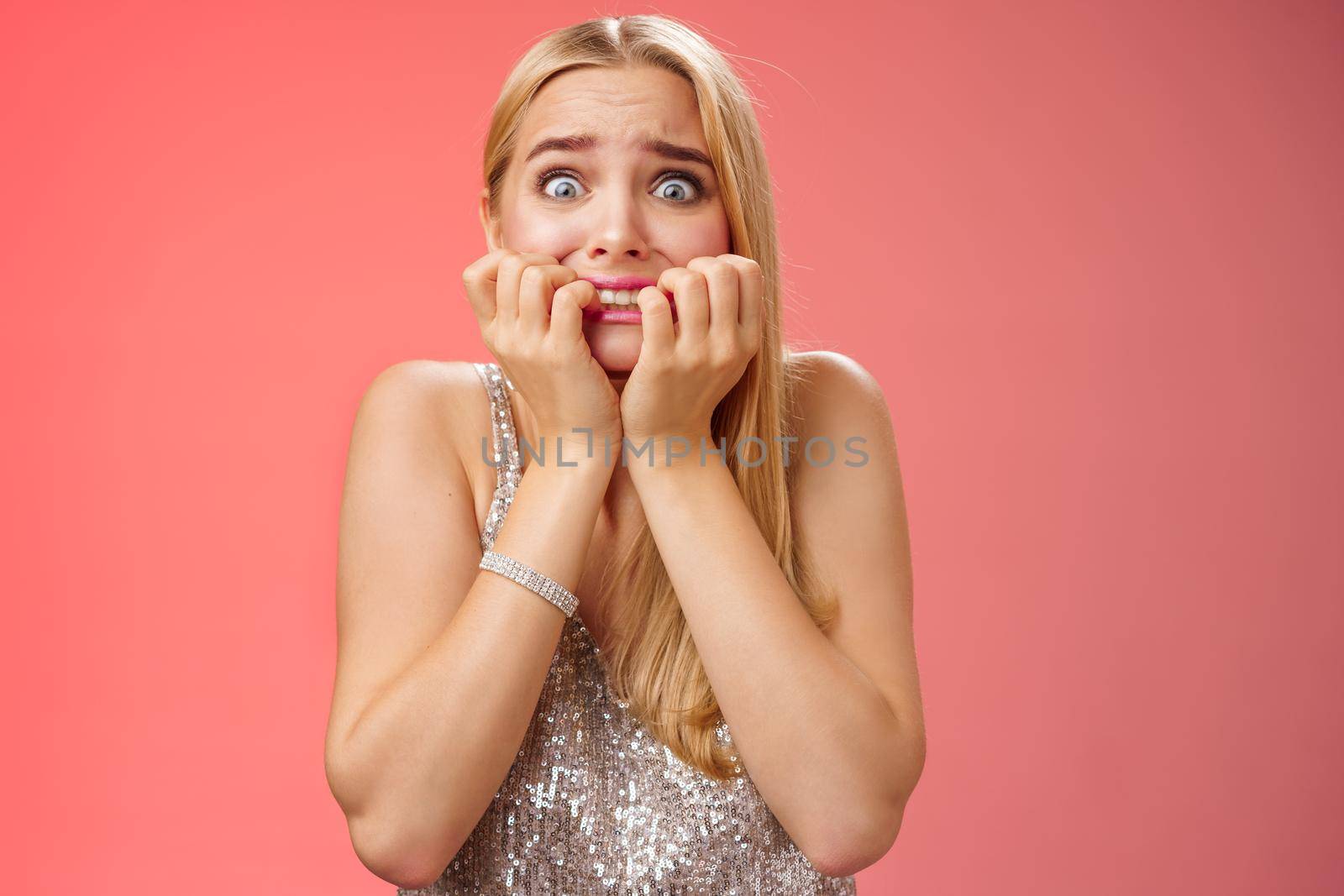 Frightened afraid panicking young cute blond woman biting nails pop eyes scared camera look terrified stunned speechless stare forward standing red background gasping trembling fear.