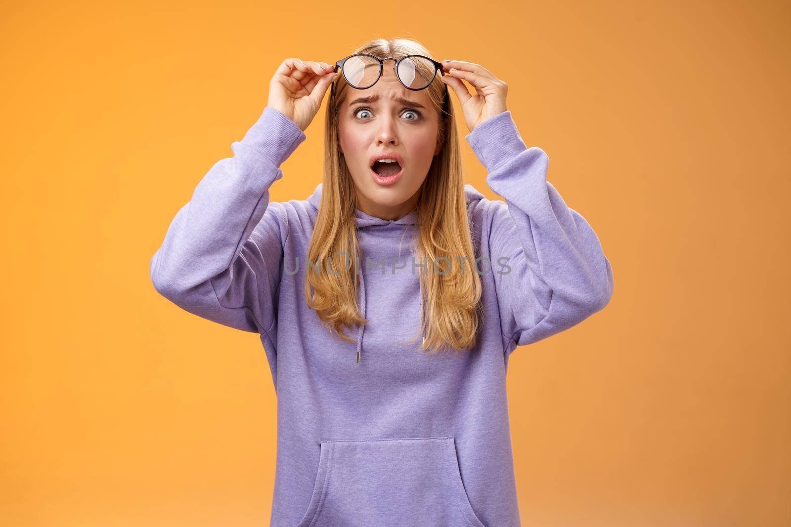 Shocked concerned young woman looking student ruin work staring disturbed upset take-off glasses popping eyes camera gasping speechless terrible acciddent happened, orange background.